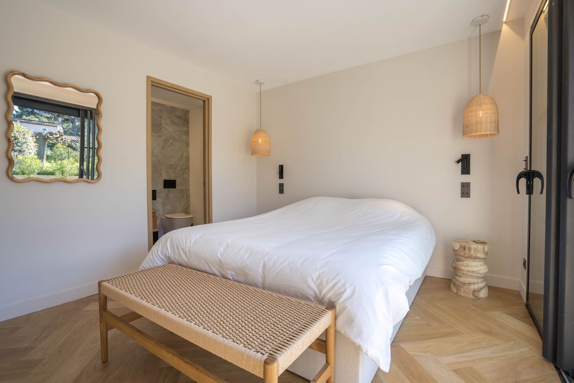 Bedroom with an oval wall mirror and woven bench at the foot of the bed