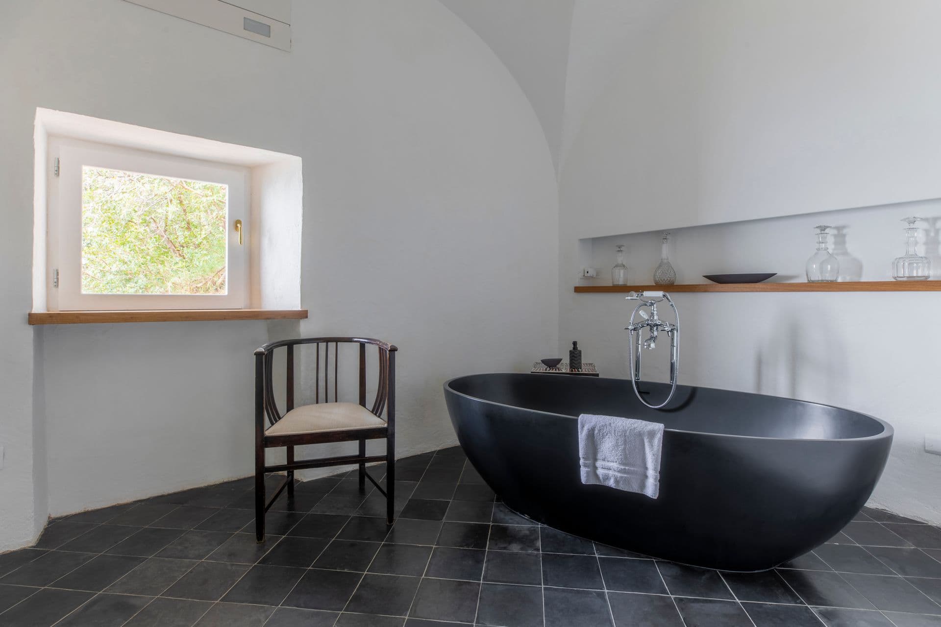 Bathroom with a freestanding black stone bathtub beside a window seat