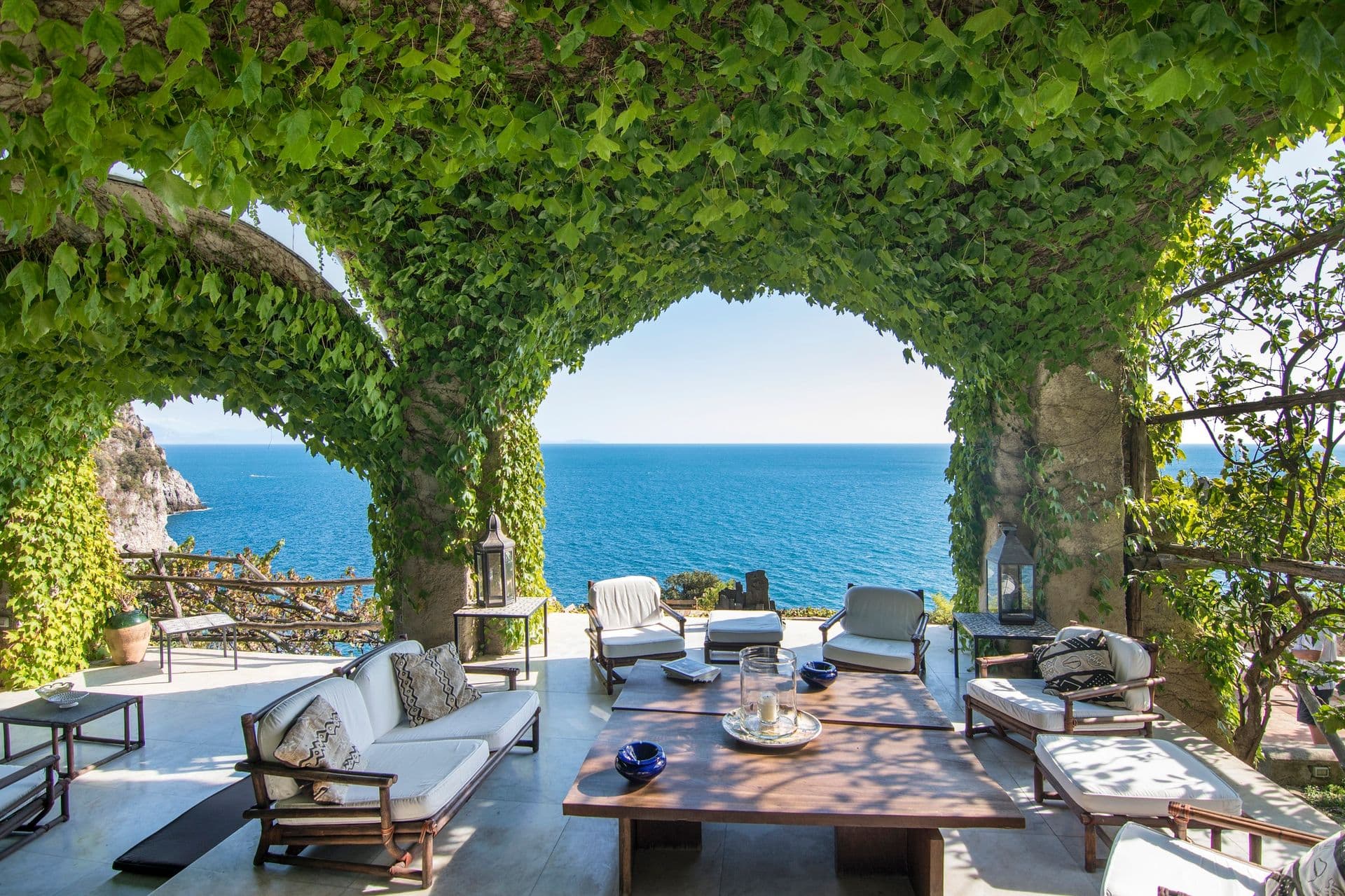 Ivy-covered stone arches framing lounge seating and the Amalfi coastline