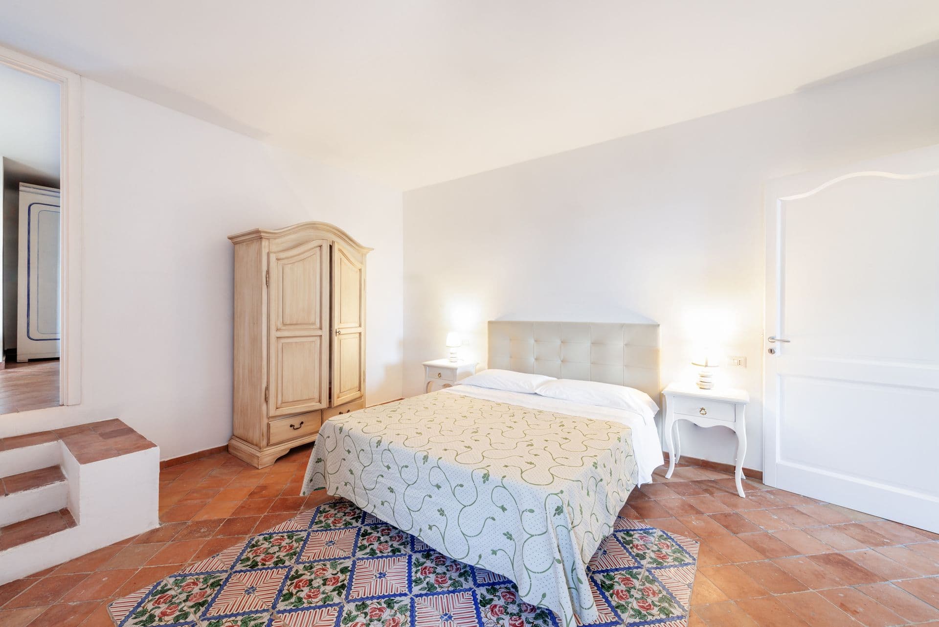 Double bedroom with a painted armoire and patterned tiled rug at Arch Above the Sea, Amalfi Coast