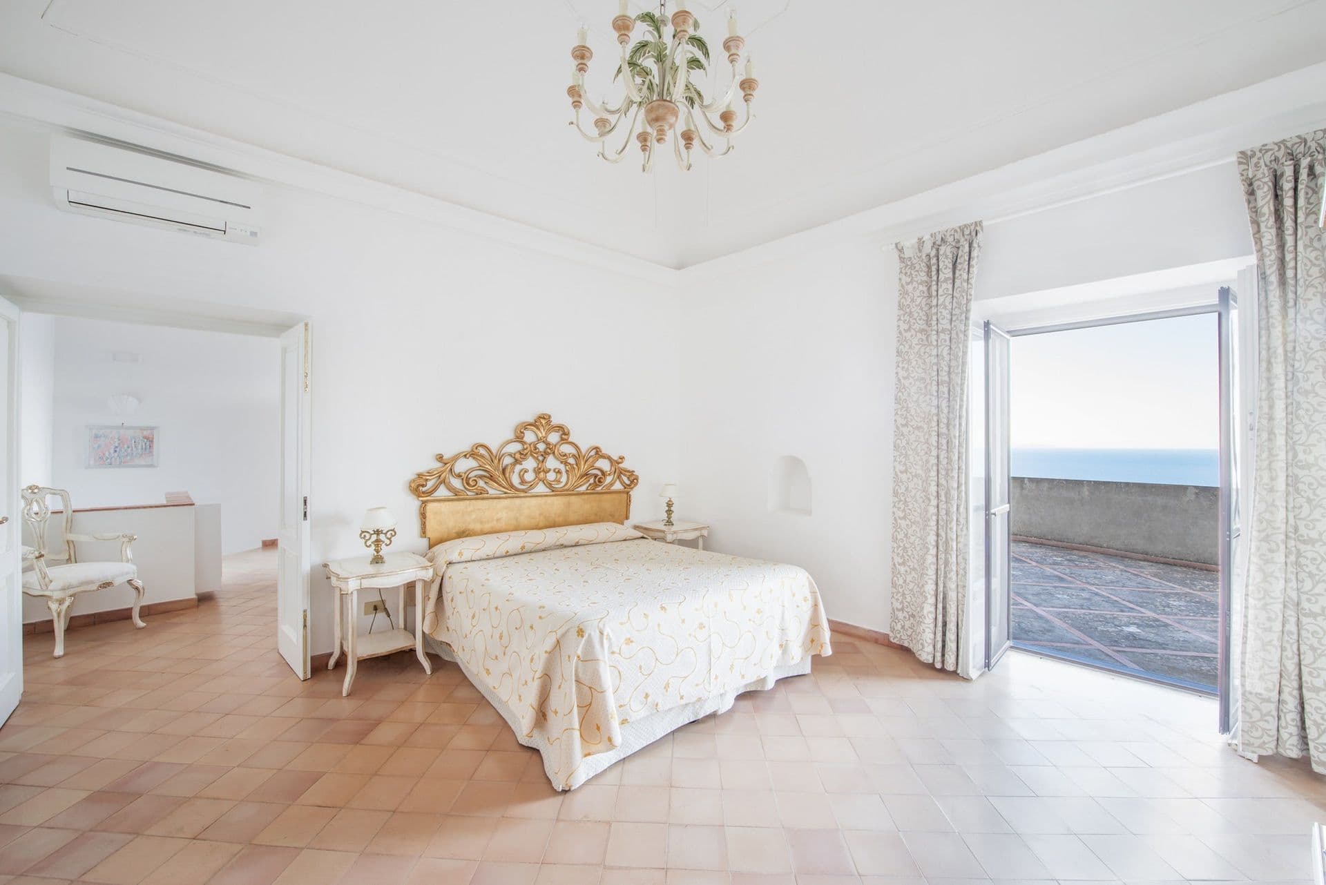 Master bedroom with a gilt headboard and doors to a sea-view terrace at Arch Above the Sea, Amalfi Coast