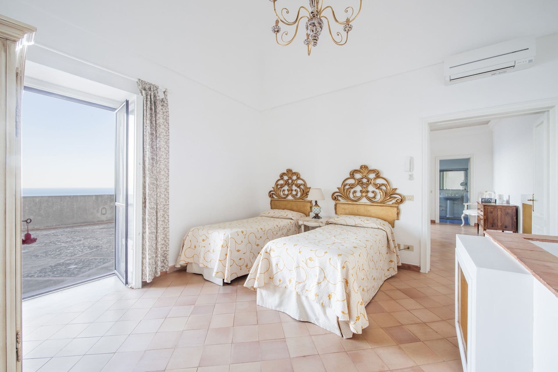 Twin bedroom with gilt headboards opening to a sea terrace at Arch Above the Sea, Amalfi Coast