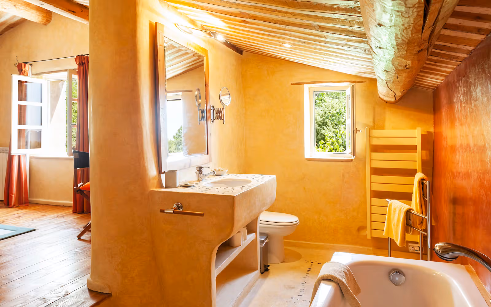 Ochre tadelakt bathroom with a moulded vanity and tub under the eaves at Choral Words, Var, Provence