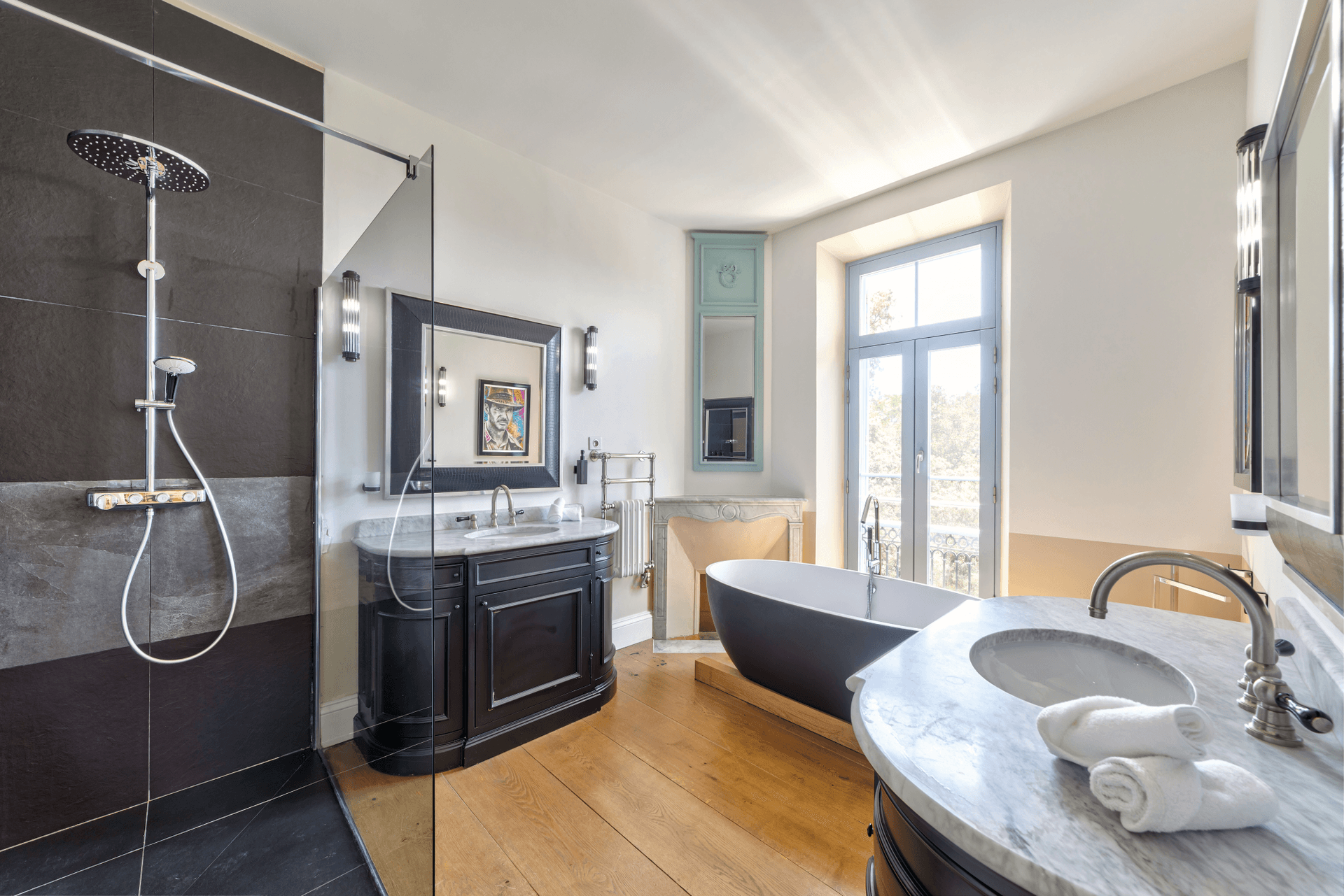 A freestanding black bath beside a marble fireplace and walk in shower