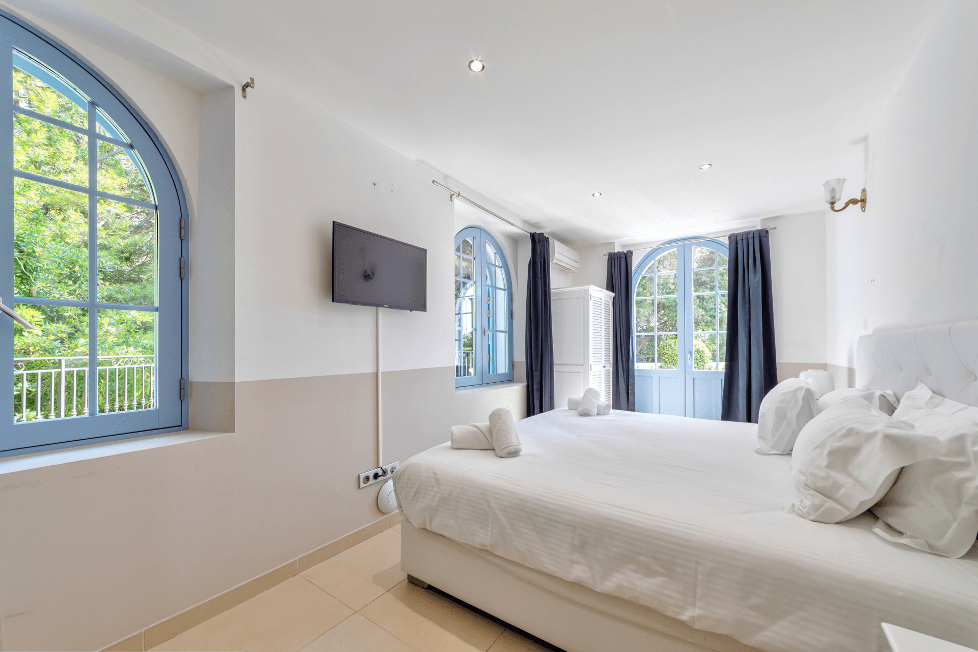 A bedroom with pale blue joinery and an arched window overlooking the gardens