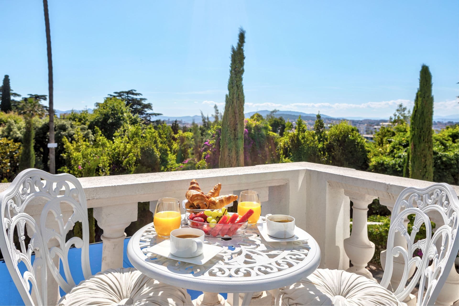 A wrought iron breakfast table laid with fruit and pastries on the villa's terrace