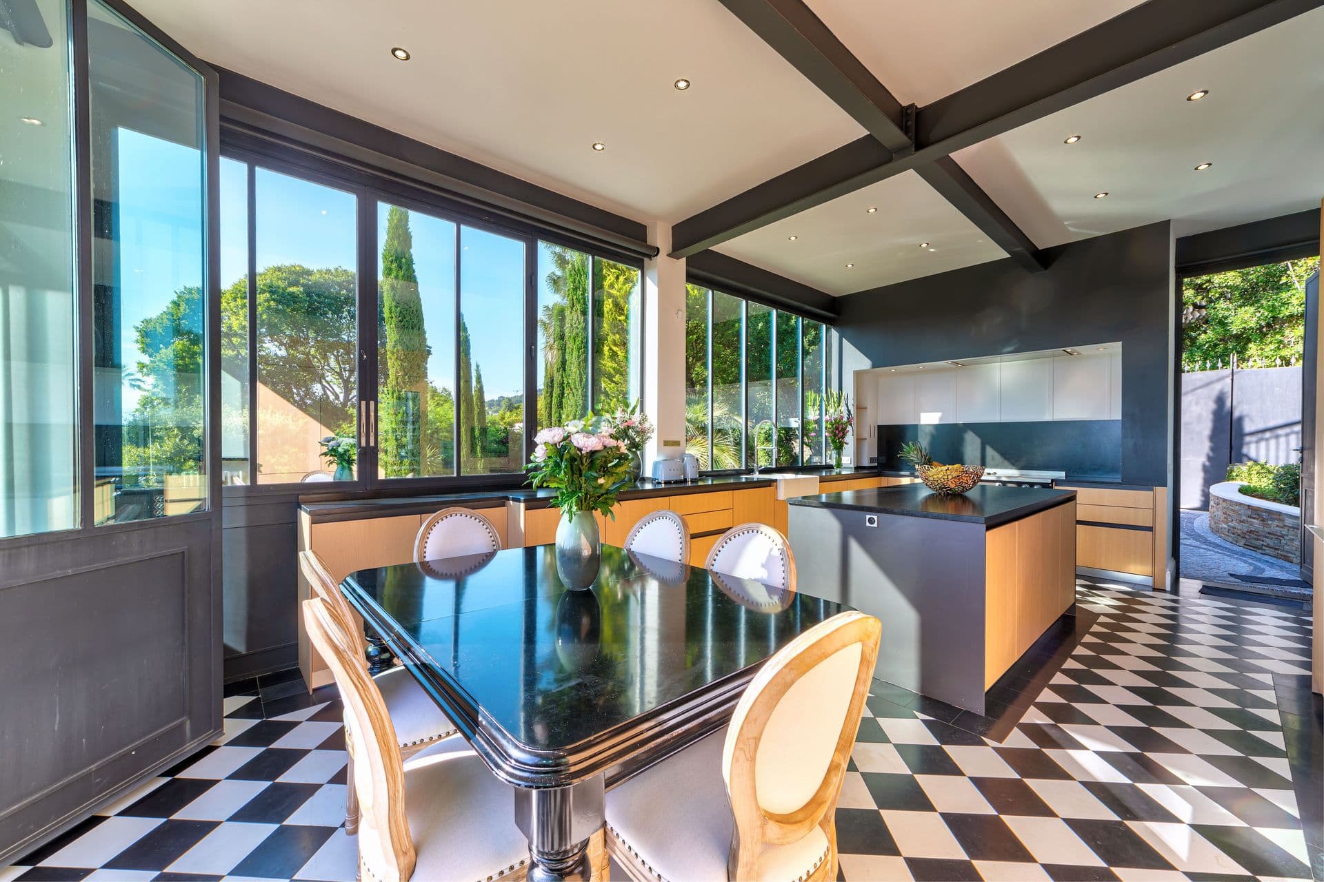 An open plan kitchen and dining area with black and white chequered flooring and glazed walls