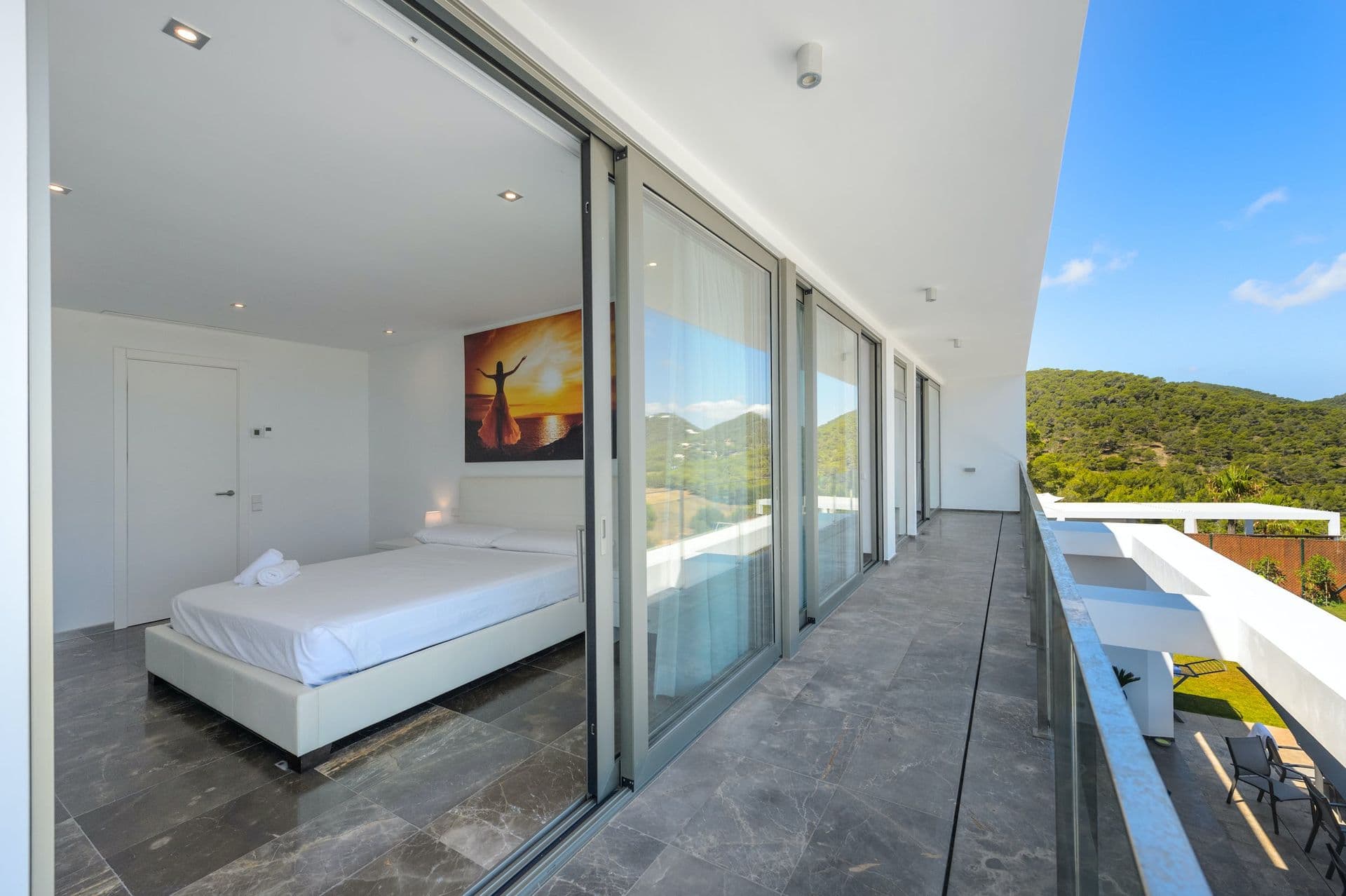 Bedroom with full-height glass sliding doors opening onto a hillside-view balcony