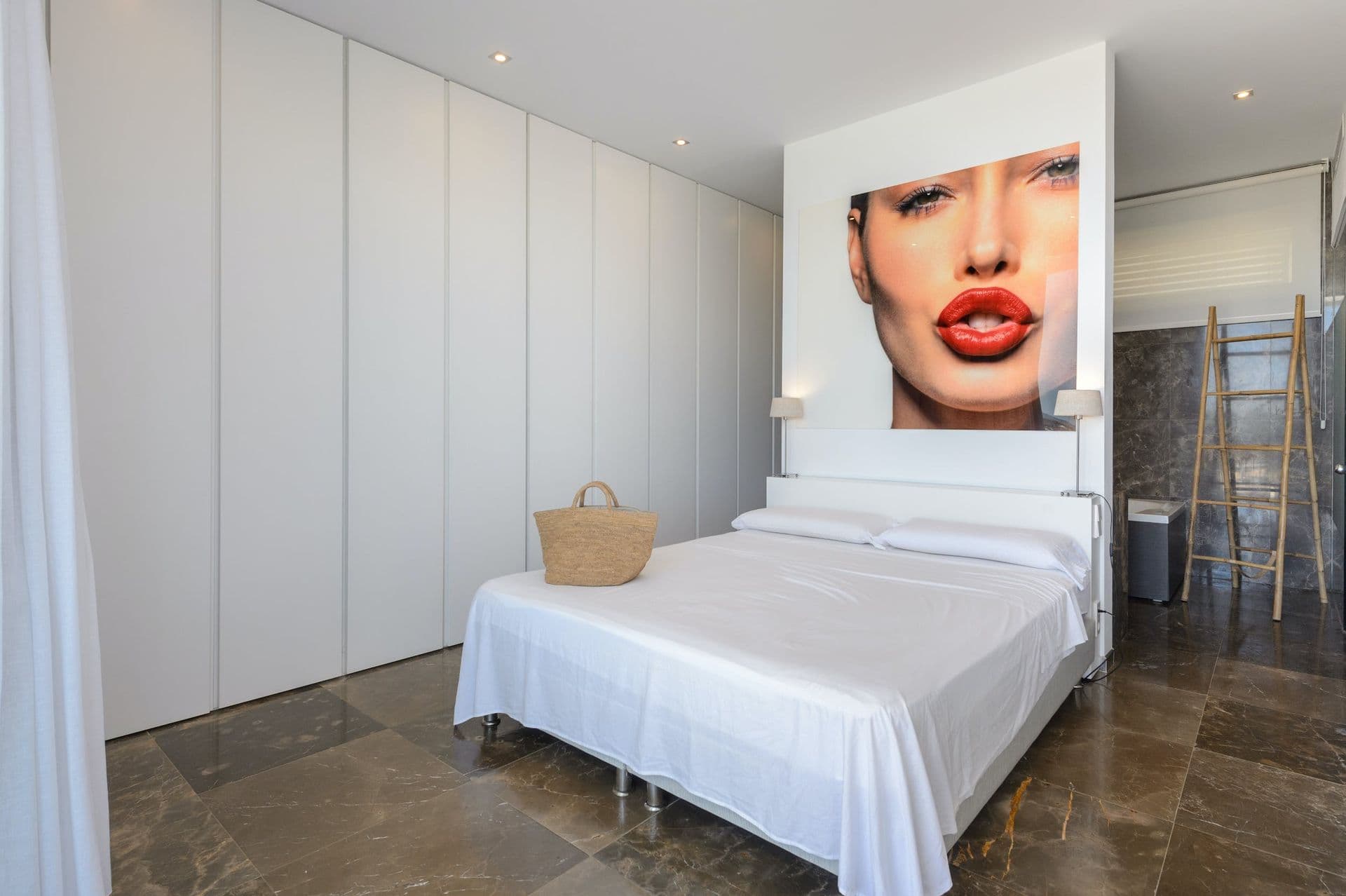 Bedroom with a large pop-art portrait above the bed and marble-tiled walls