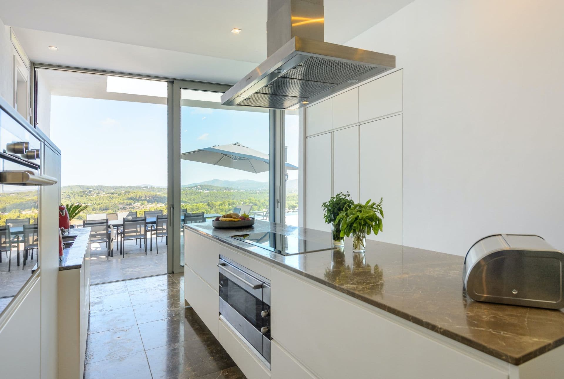 White kitchen island with an outdoor dining terrace and hillside view beyond
