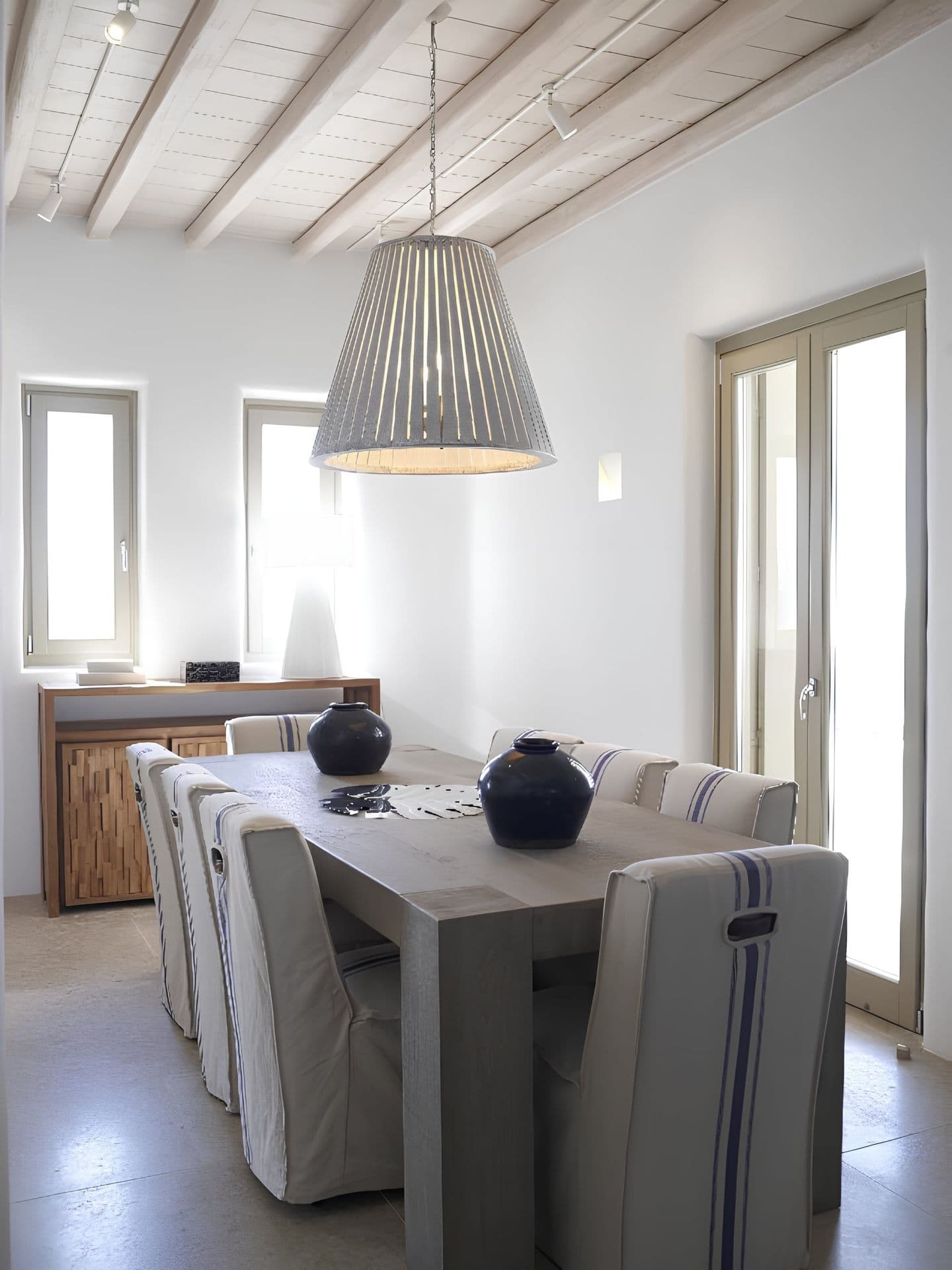 Dining table beneath exposed wood beams and a linen shade pendant.