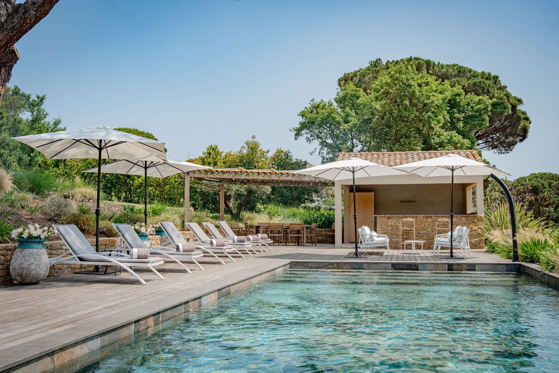Pool deck with sun loungers, parasols and a shaded cabana.