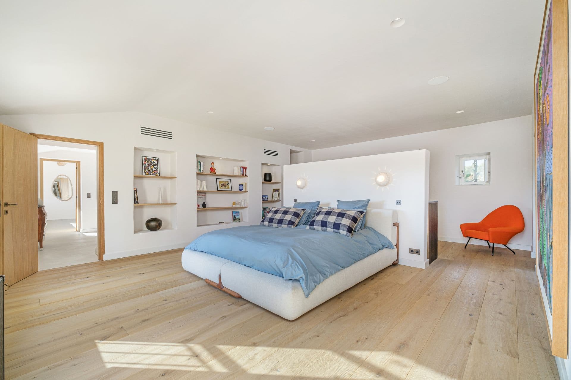Bedroom with blue bedding opening onto a dressing area with orange accent chairs