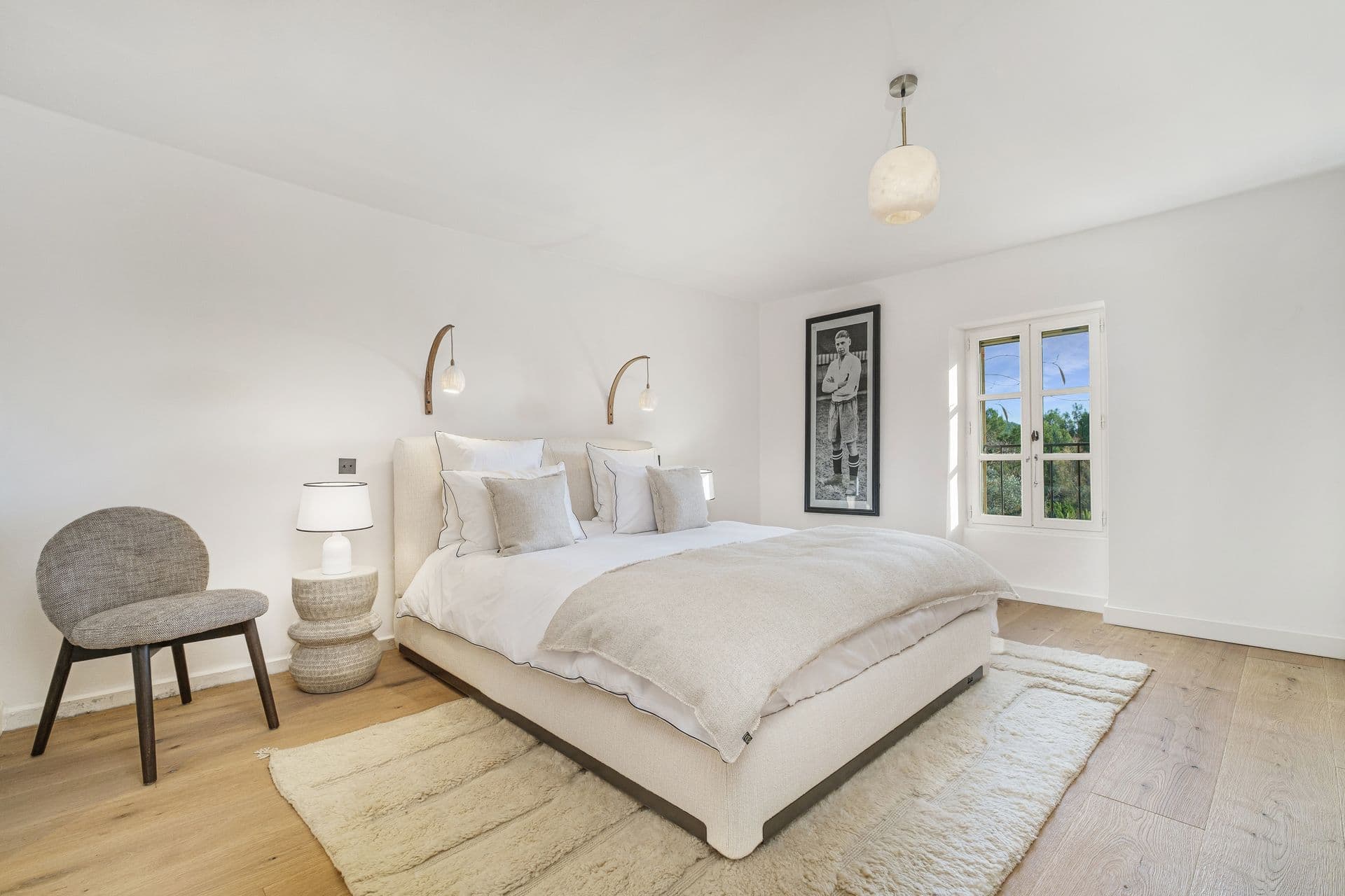 Bedroom in soft neutral tones with a statement pendant light and armchair