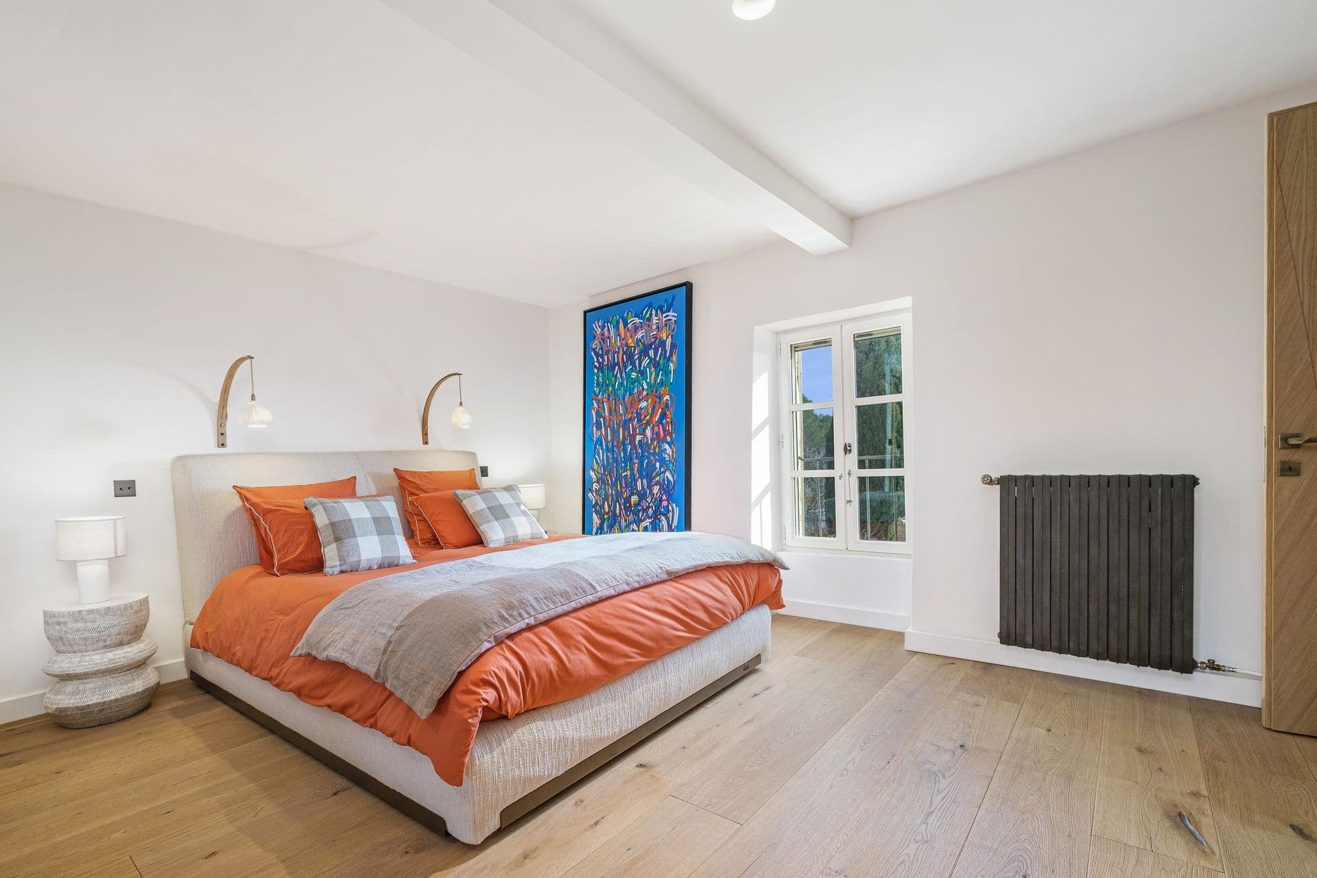 Bedroom with orange bedding, blue artwork and garden-facing windows