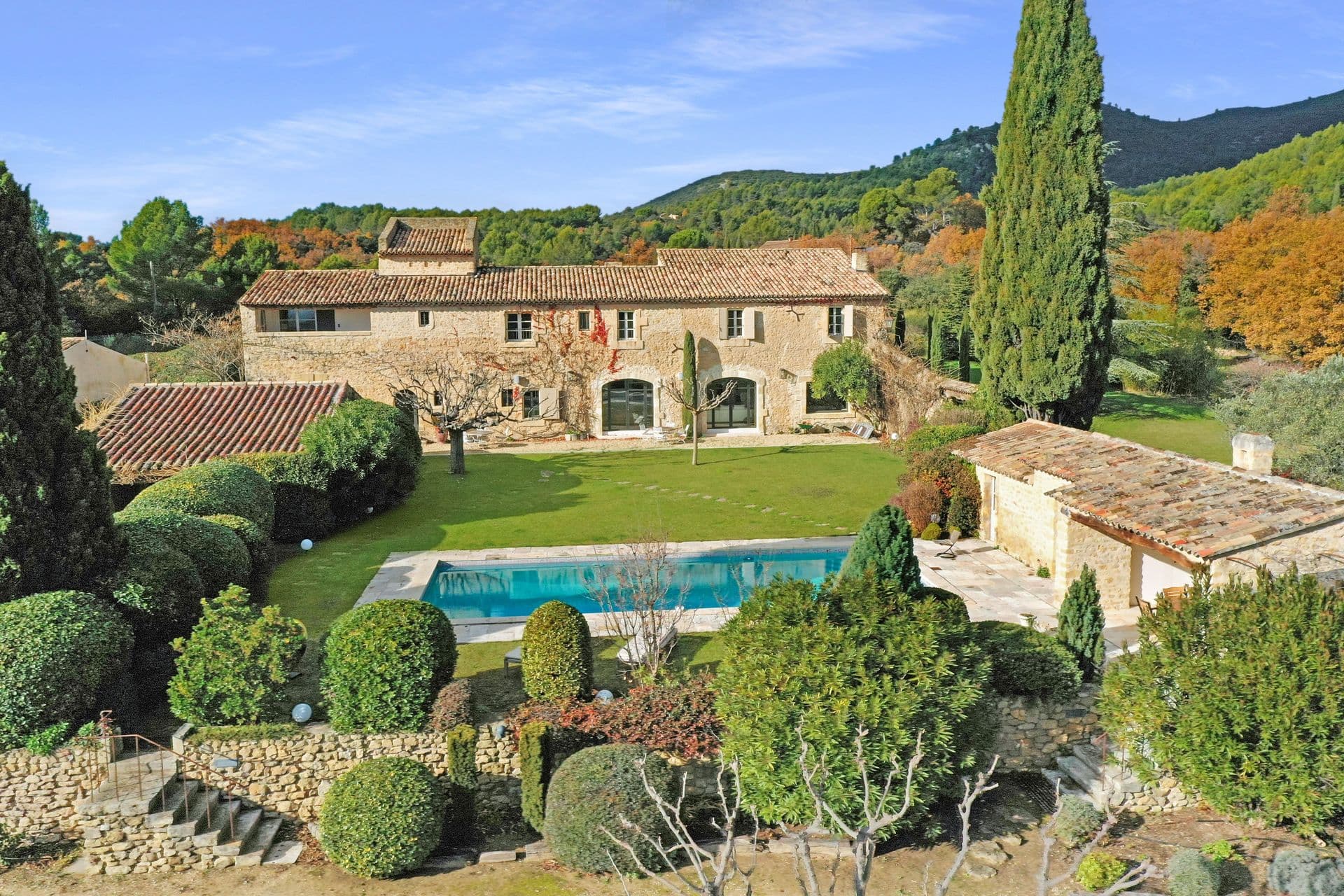Aerial view of a stone Provencal estate with swimming pool, manicured gardens and hills beyond
