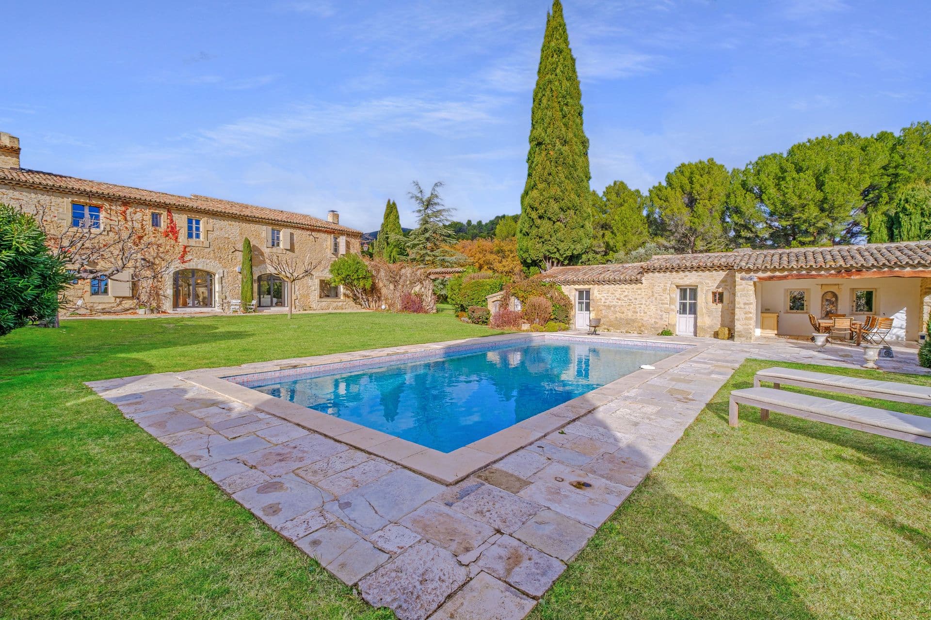Stone-edged swimming pool set into a manicured lawn beside the farmhouse buildings