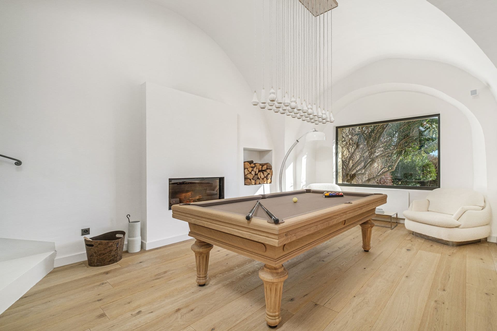 Billiards room with a wooden pool table beneath a vaulted ceiling and garden views
