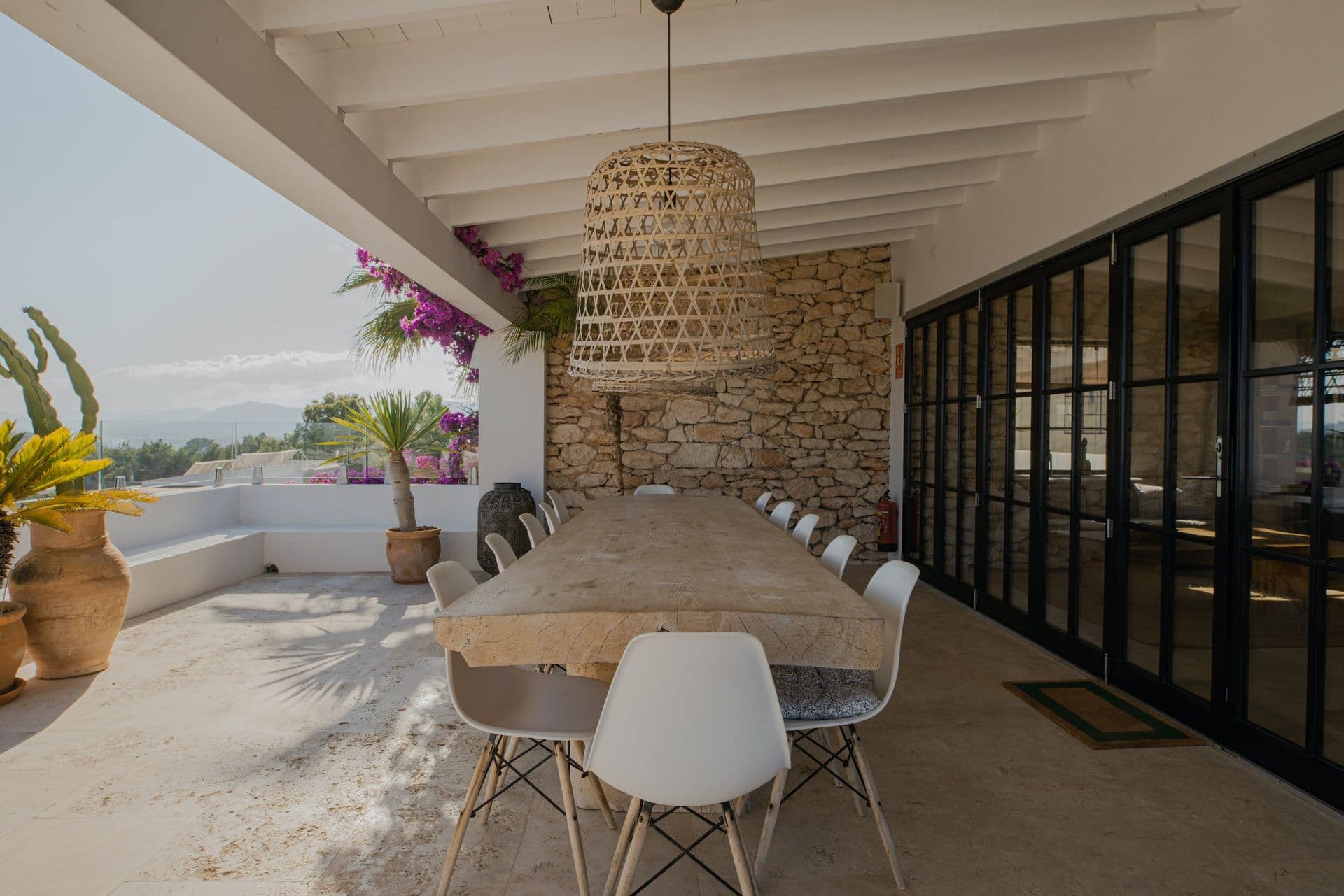 Long wooden dining table beneath a covered stone pillared terrace at New Beat