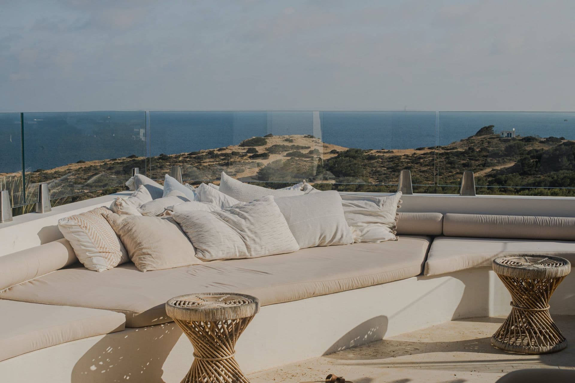 Low white outdoor sofa piled with cushions on a terrace overlooking the sea at New Beat