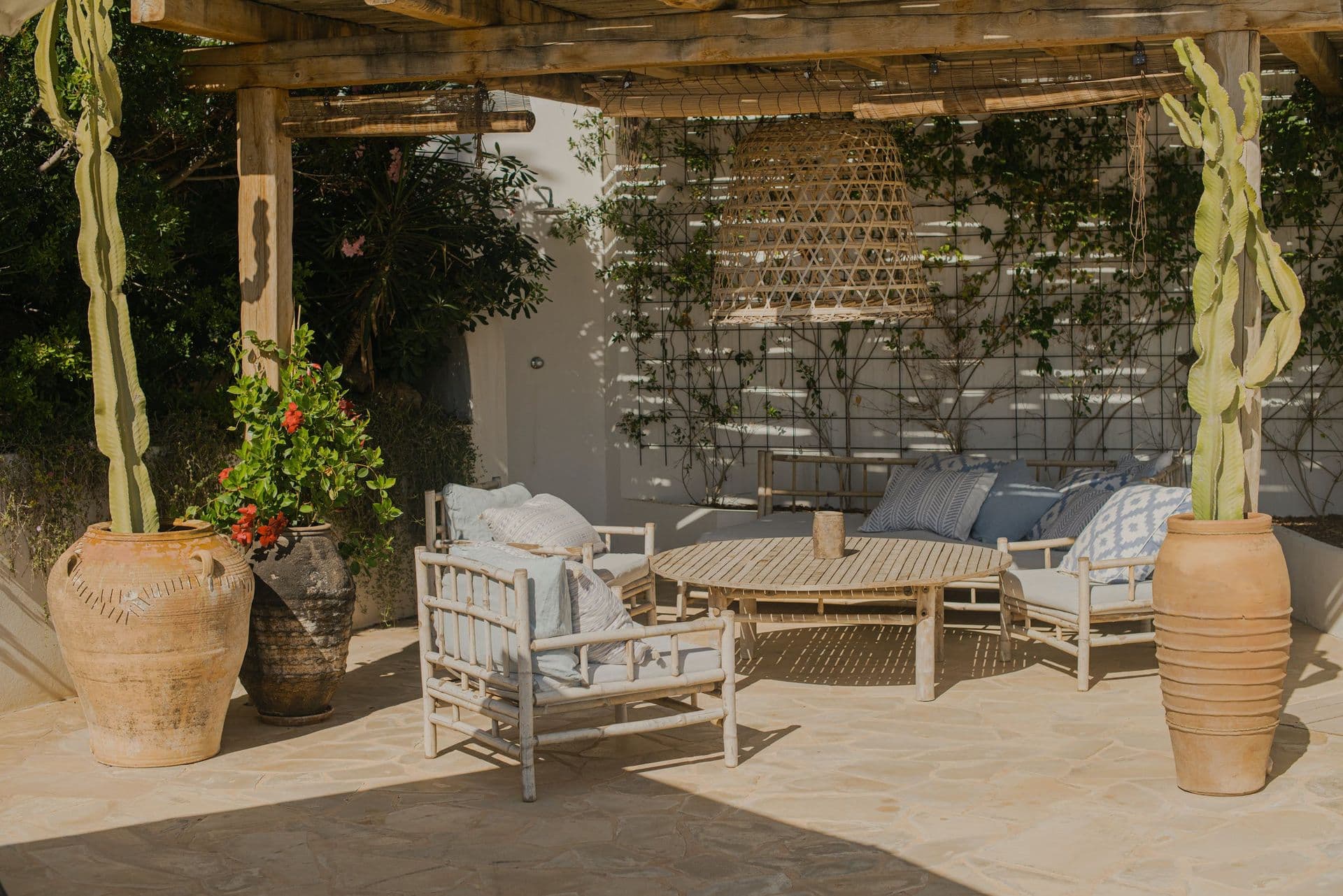 Woven lounge chairs beneath a wooden pergola surrounded by potted cacti at New Beat