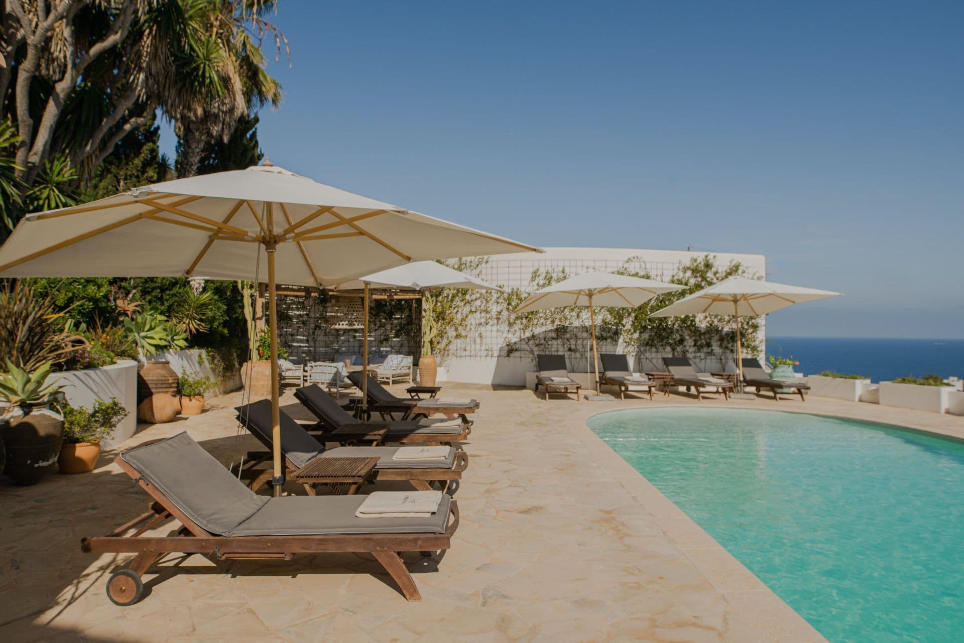 Timber sun loungers lined along the edge of a turquoise swimming pool at New Beat