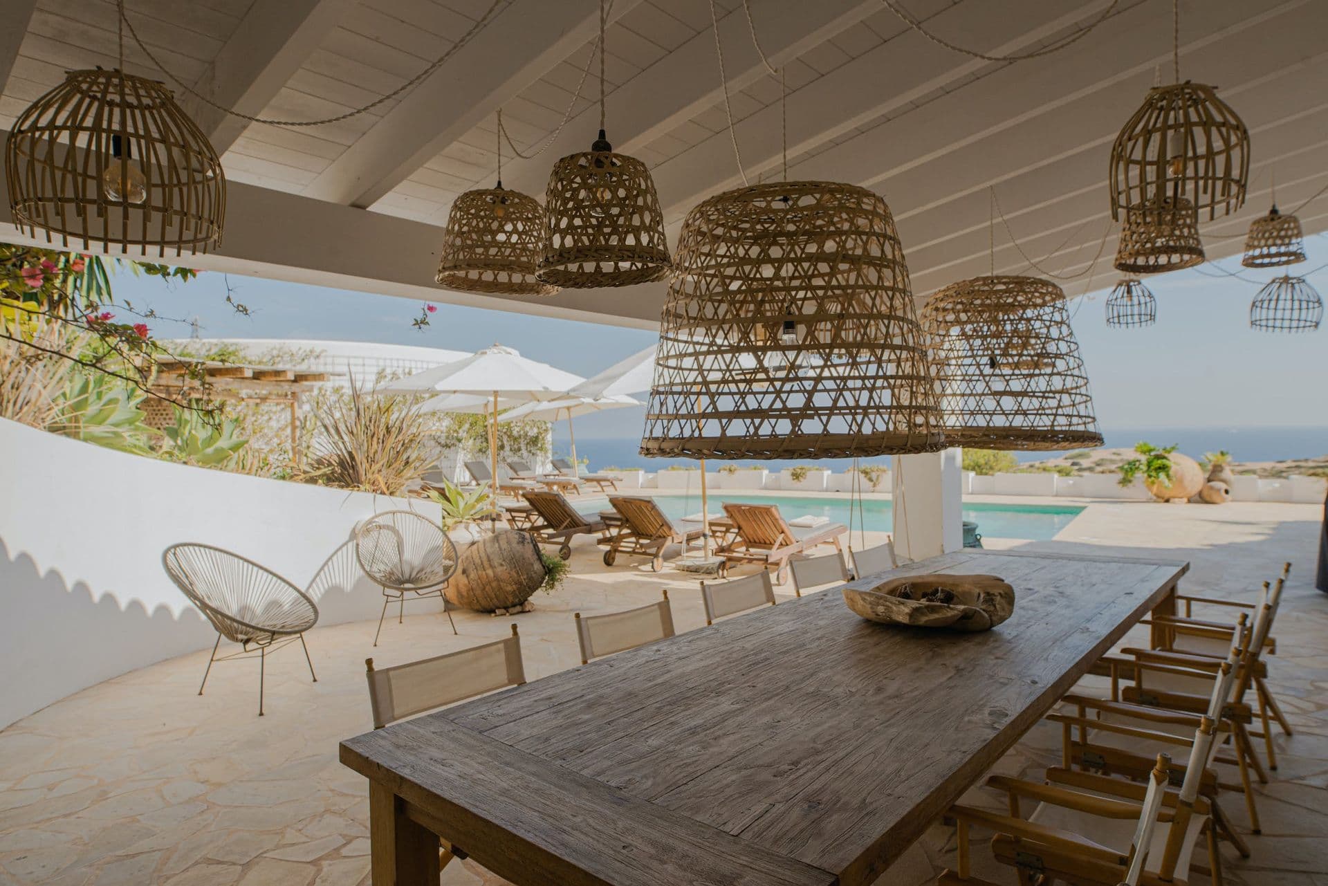 Outdoor dining table beneath woven pendant lights with the pool visible beyond at New Beat