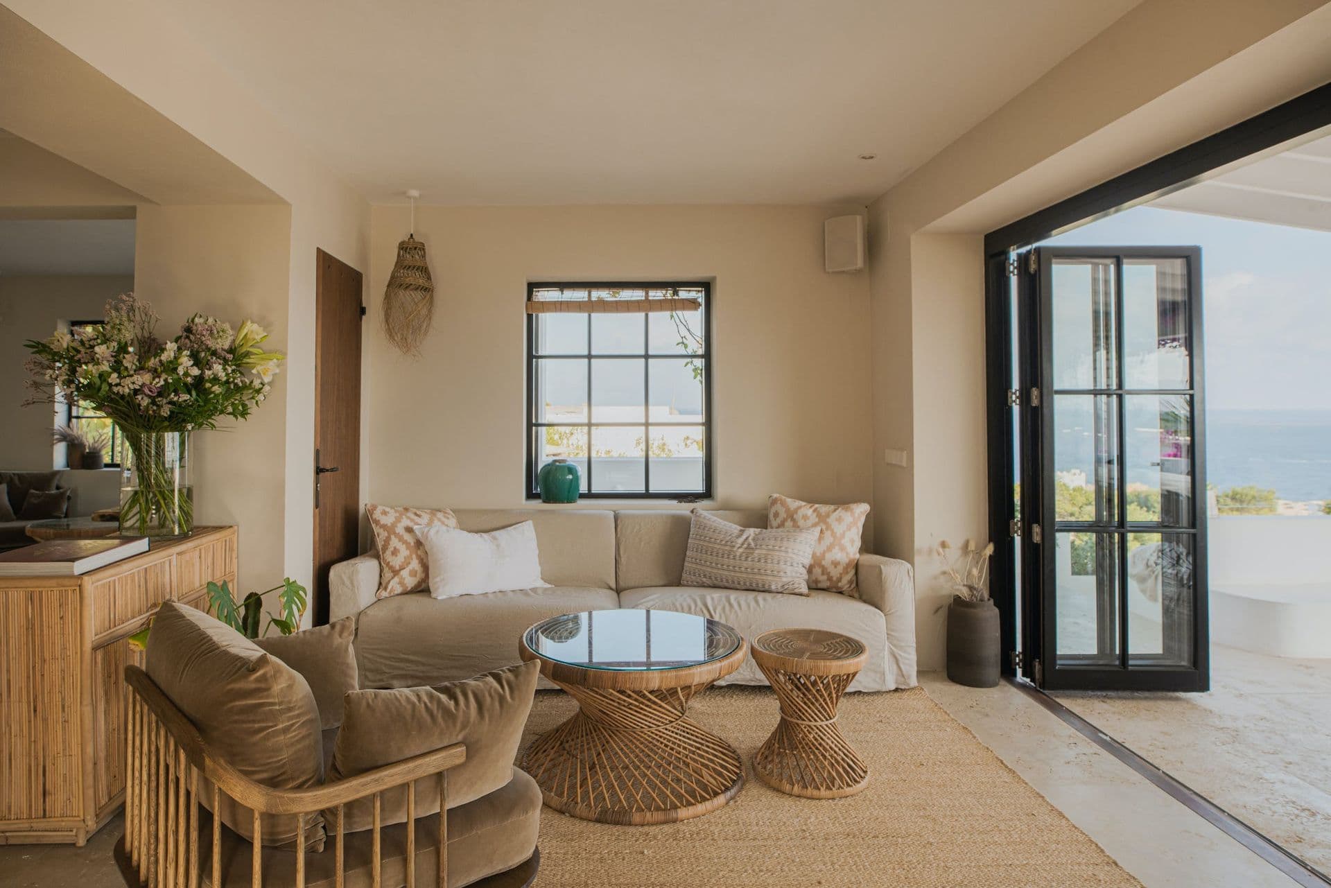 Neutral toned living room opening through glass doors onto a terrace with sea views at New Beat