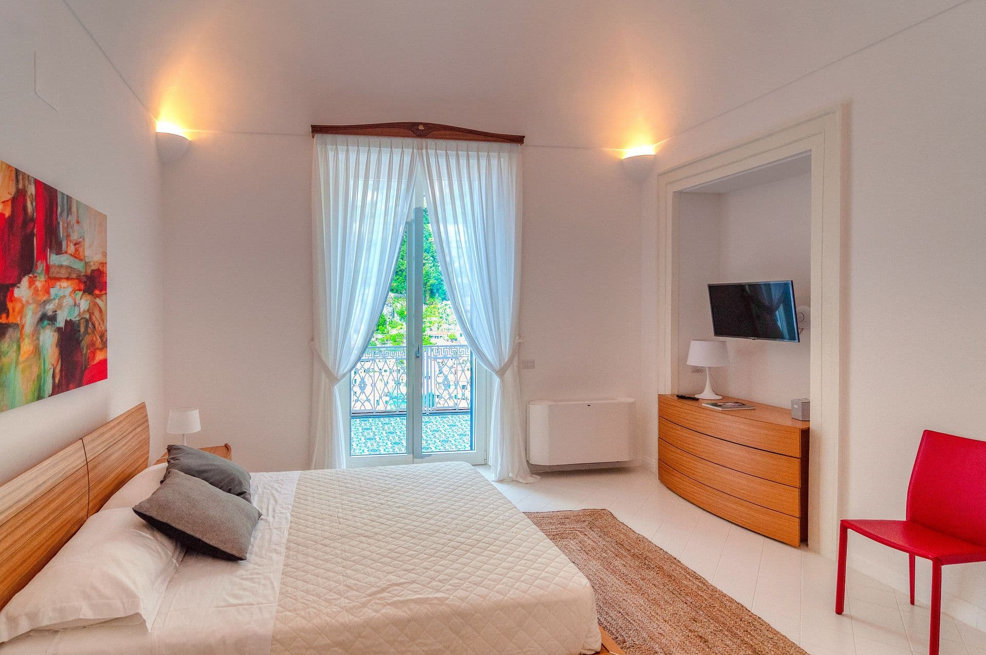 Bedroom with a colourful artwork, red accent chair and Juliet balcony
