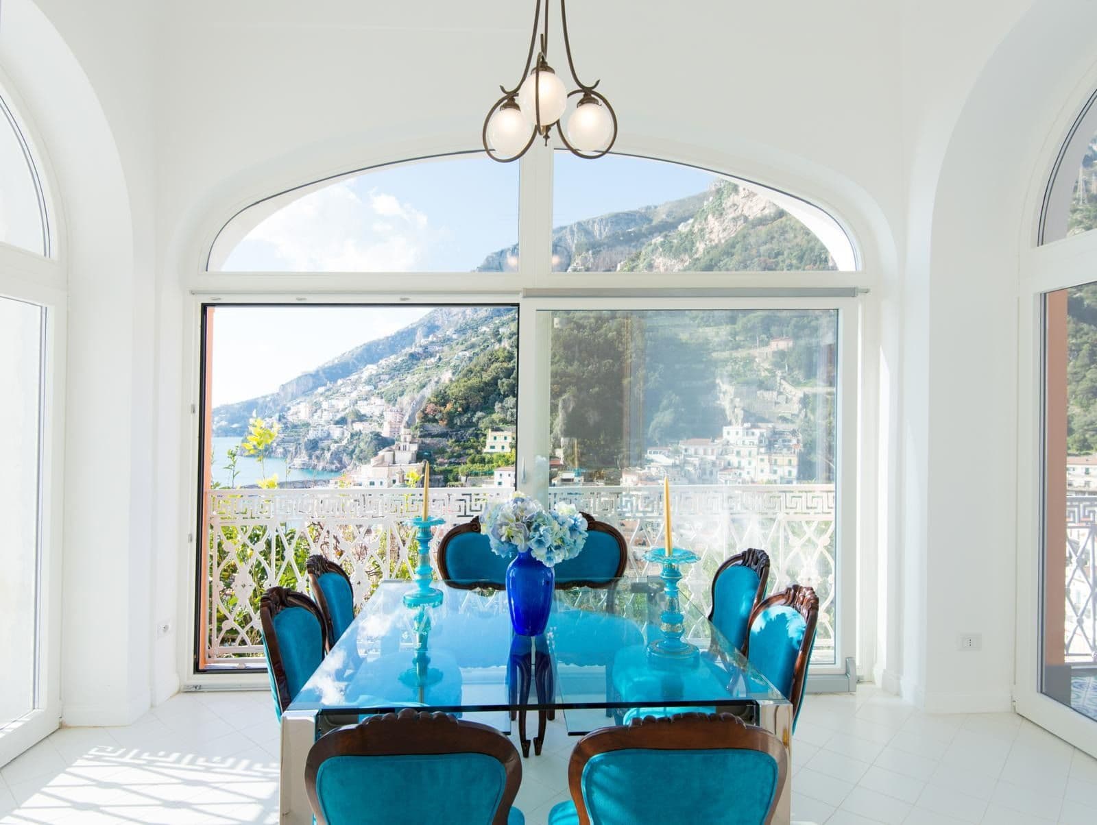 Dining room with turquoise chairs and arched windows framing the coastline