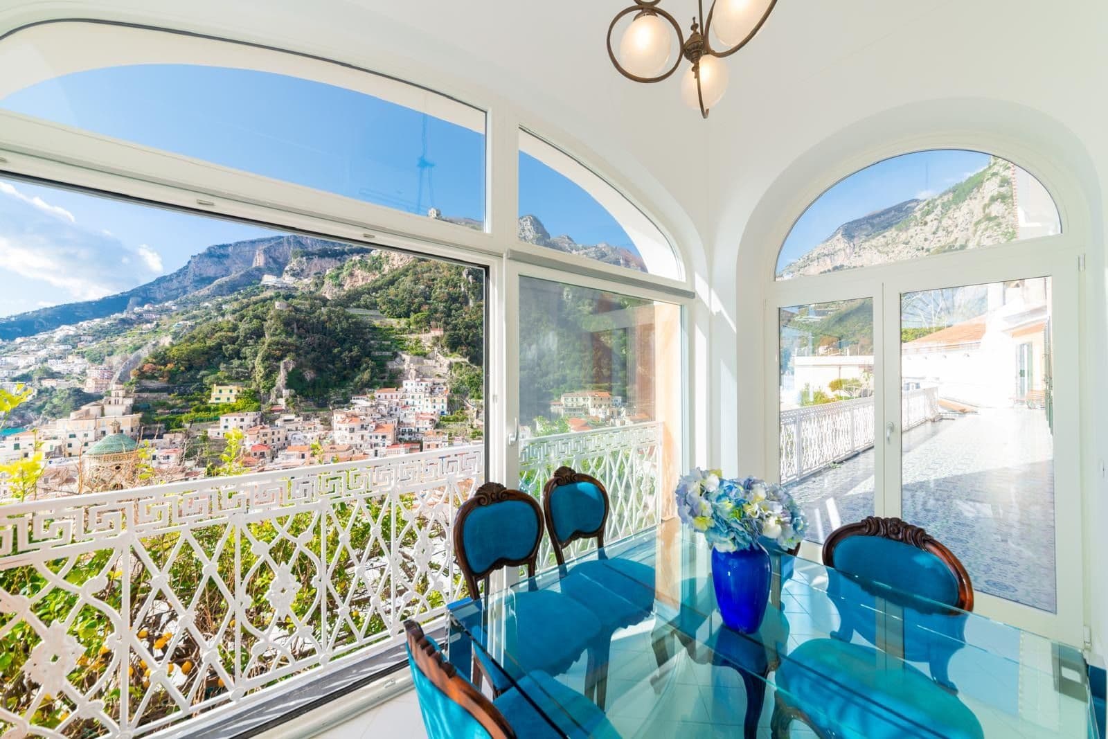 Glass dining table beneath arched windows with views over Amalfi town