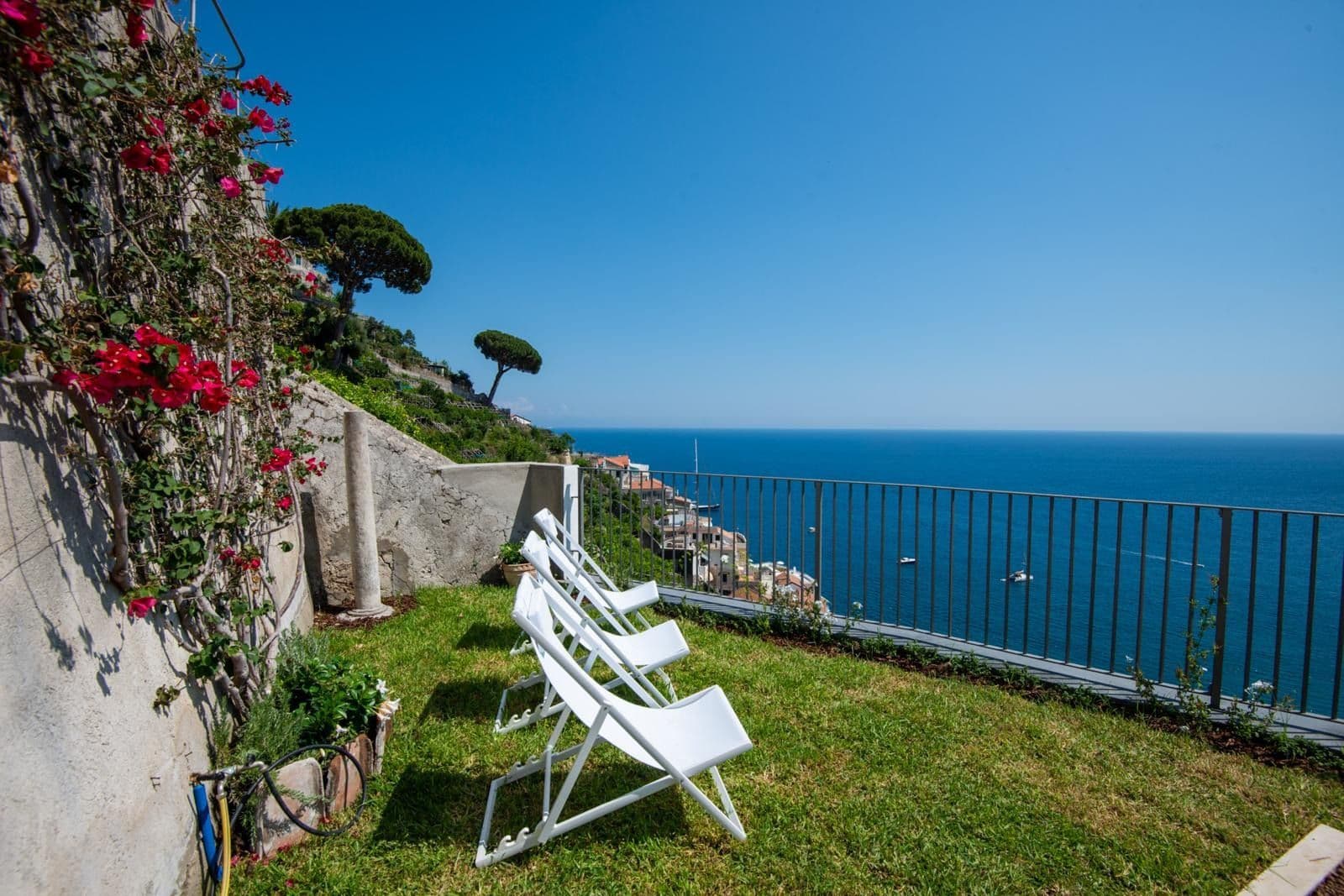 Grassy garden terrace with deck chairs and bougainvillea overlooking the sea