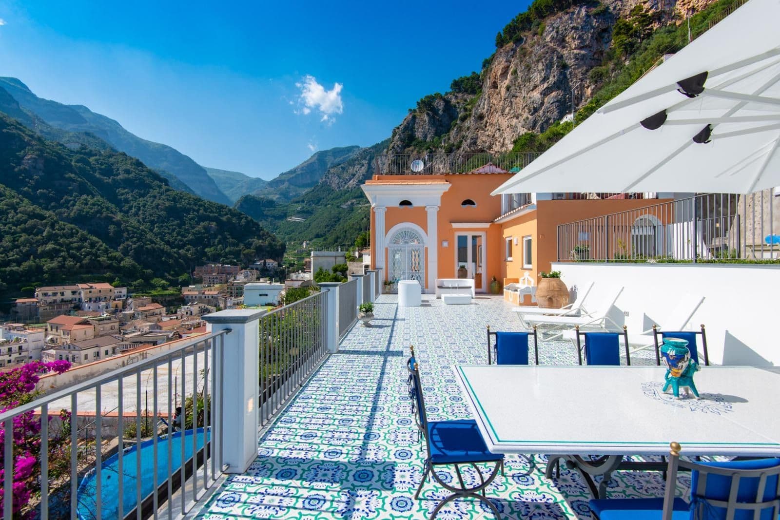 Terrace with dining tables set against the terracotta villa and coastal mountains