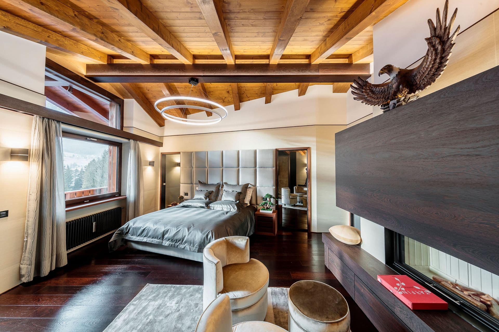 Master bedroom with a grey velvet headboard, timber ceiling and fireplace at Dolomite Prestige, Cortina d'Ampezzo
