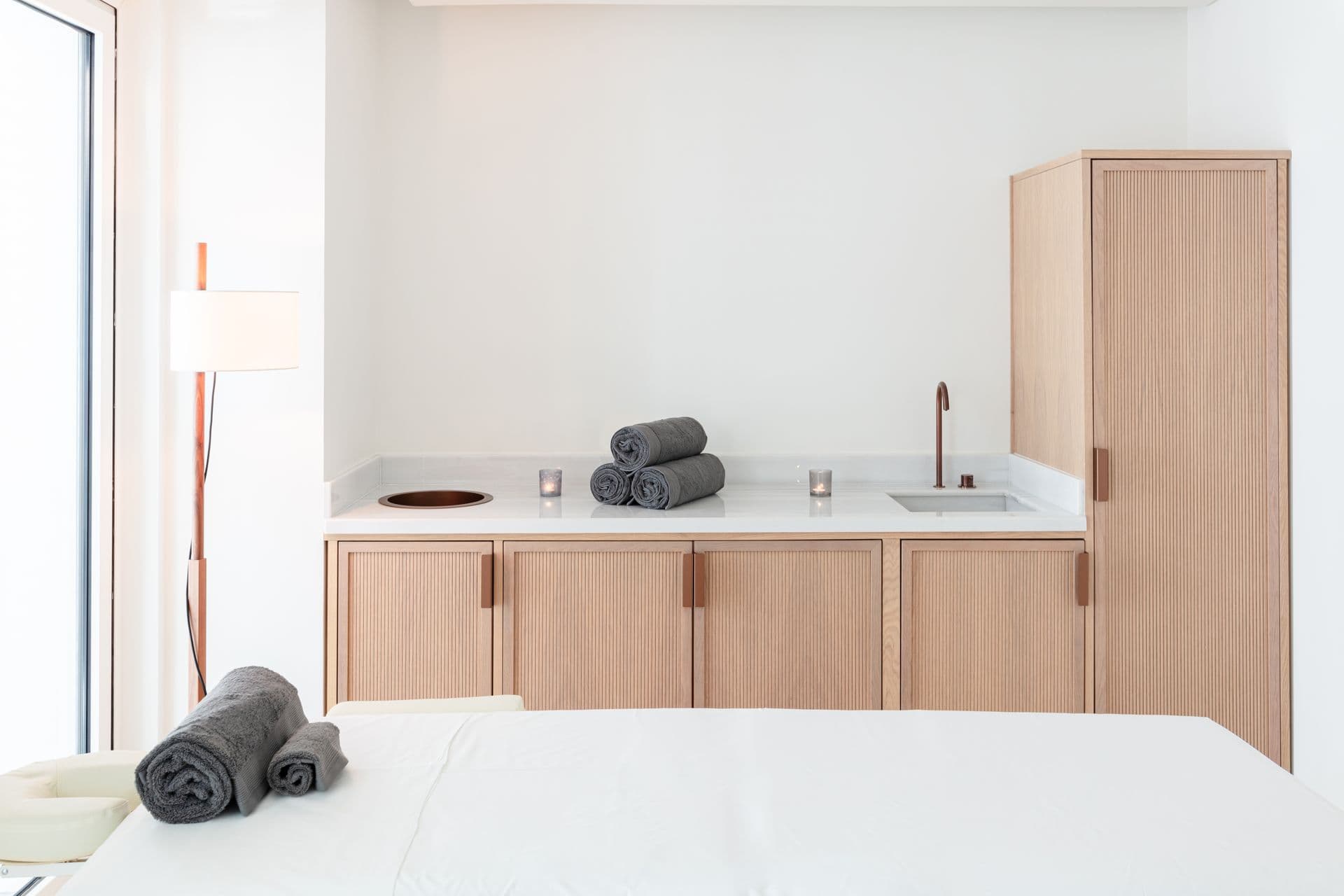 Fluted oak vanity unit with twin basins and rolled towels beside a bed