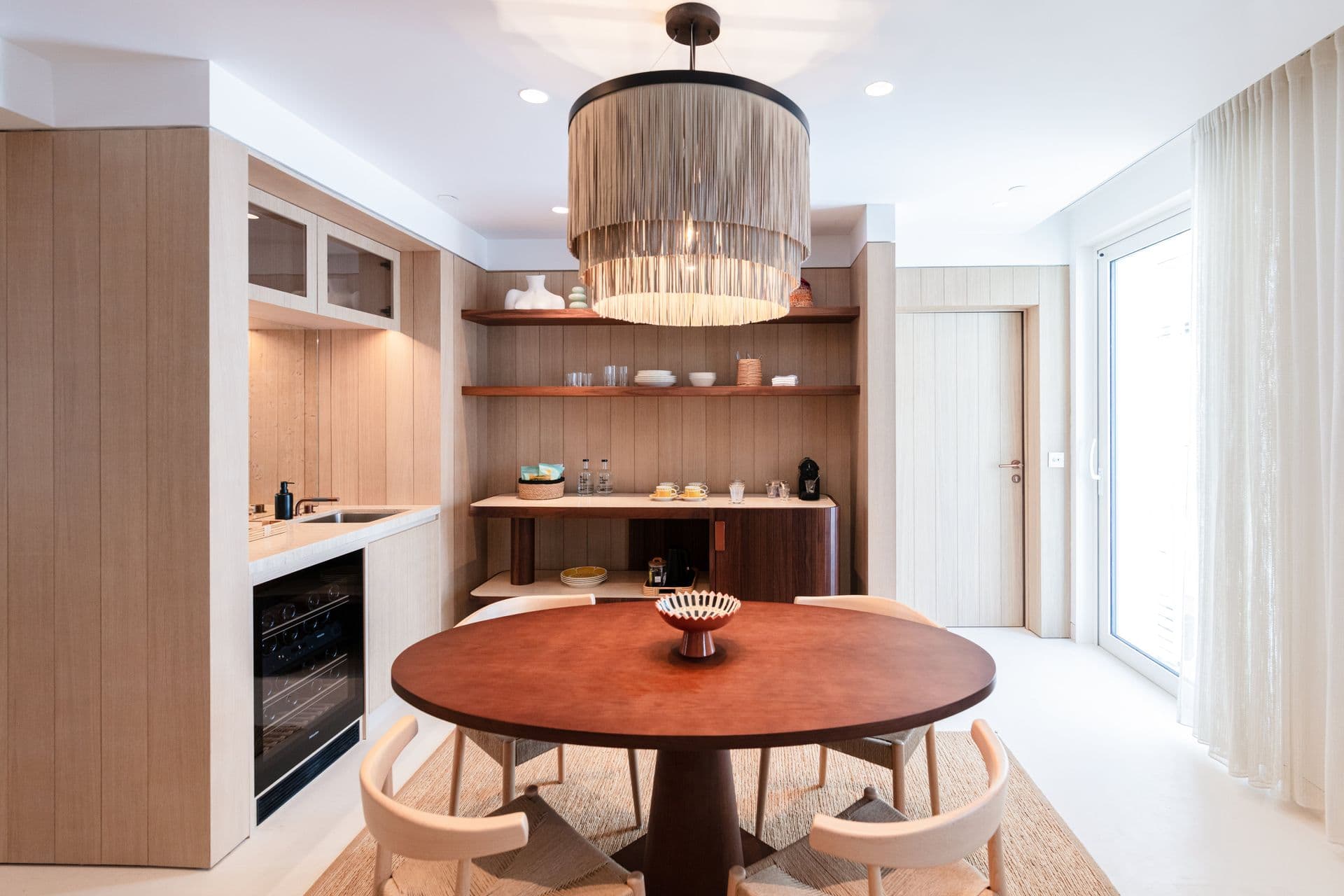 Light oak kitchen with round dining table and pendant light beside a sunlit window