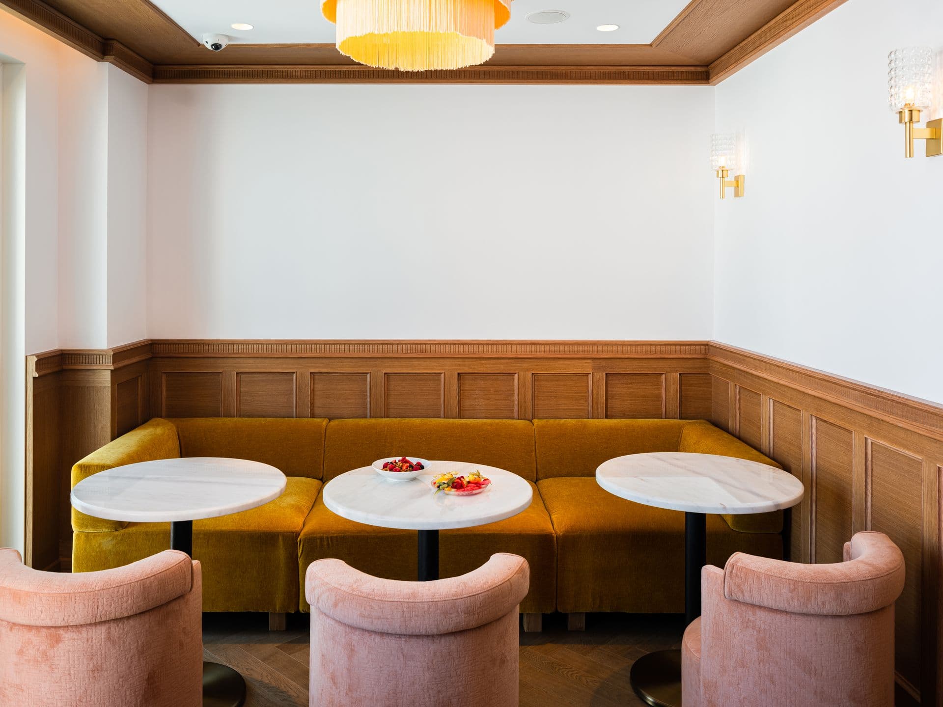 Curved pink velvet banquette seating with marble-topped tables in a warm-lit lounge