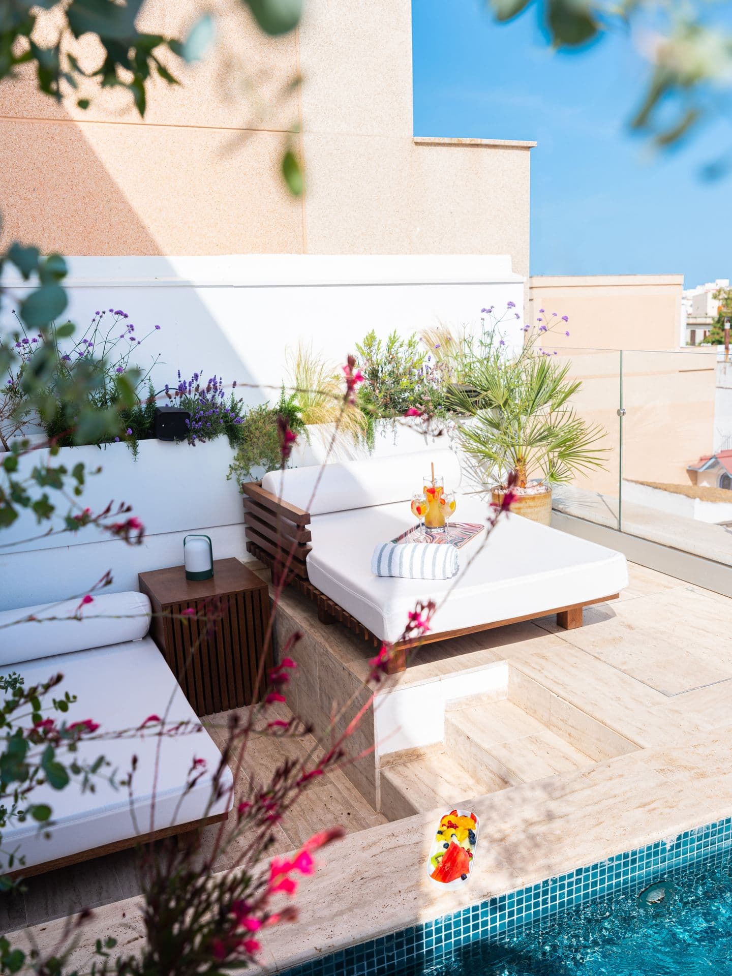 White loungers and cushioned daybed beside the rooftop pool with bougainvillea in bloom