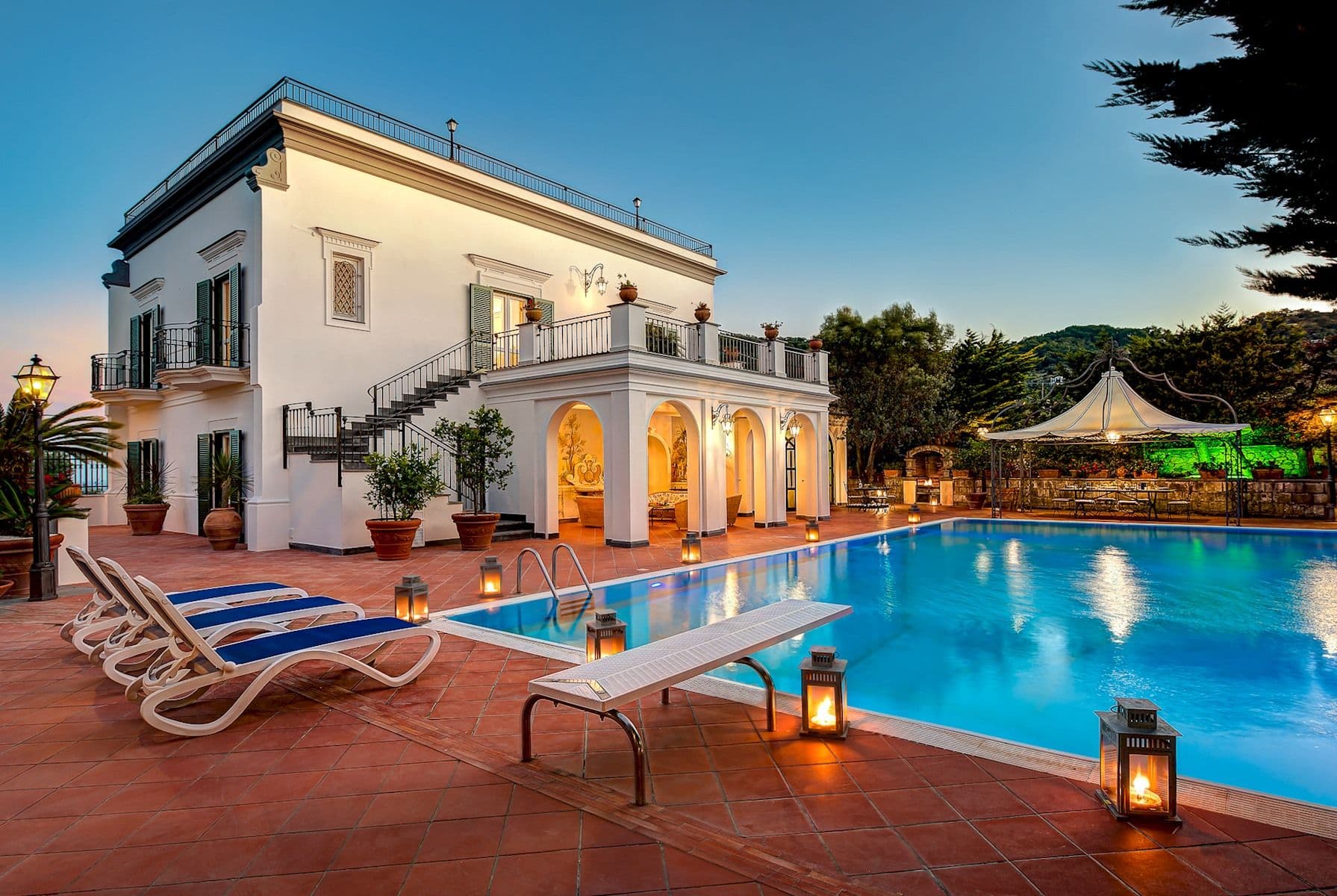 Villa facade and pool with diving board lit in the early evening.