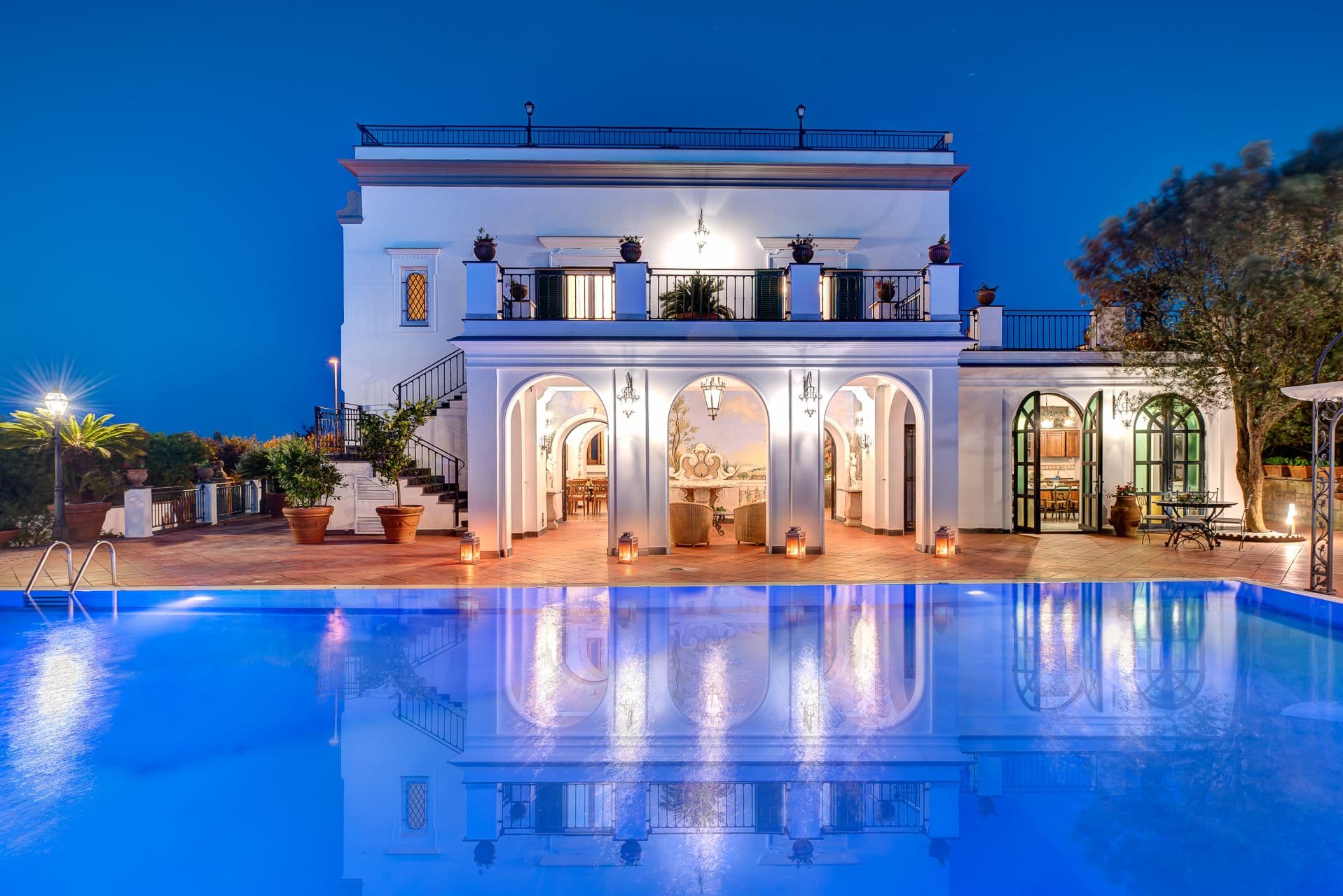 Illuminated villa and pool at twilight with reflections across the water.