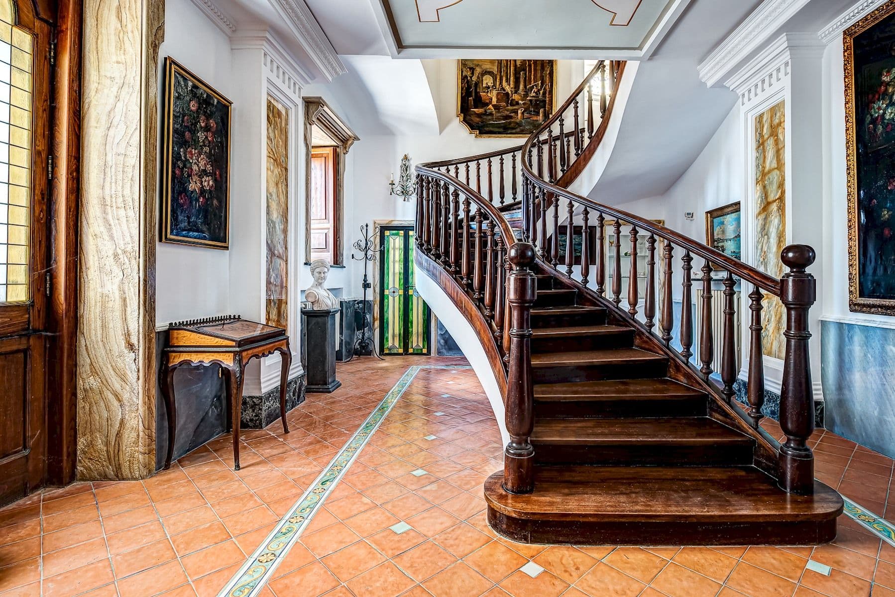 Frescoed hallway leading to a dark wood staircase.
