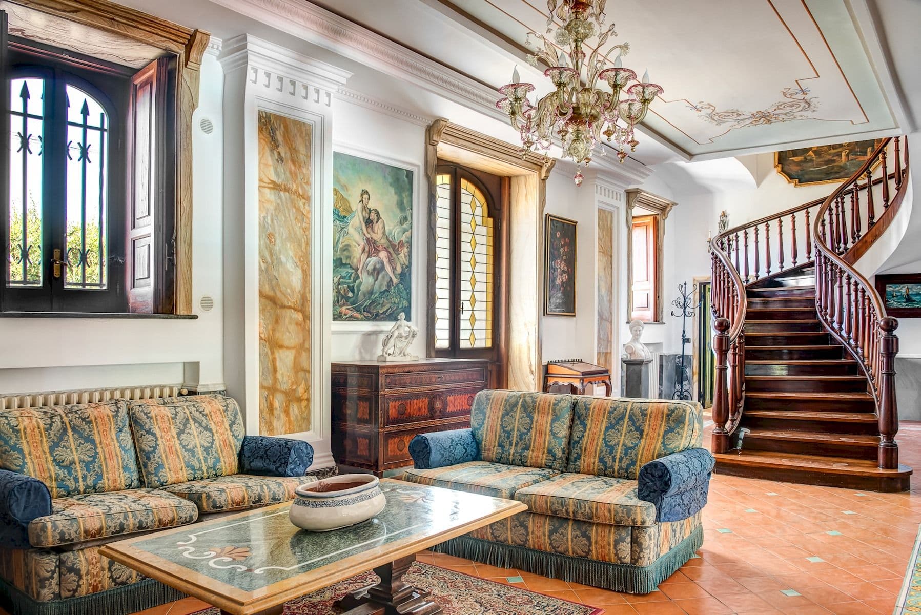 Living room with a crystal chandelier beside the sweeping staircase.