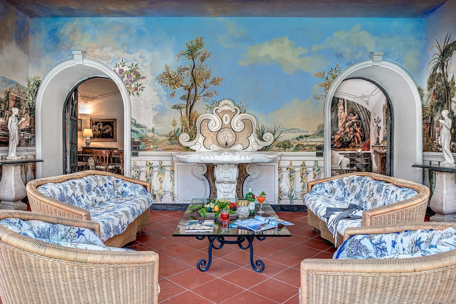 Frescoed reception room with a marble fountain mural and wicker armchairs.
