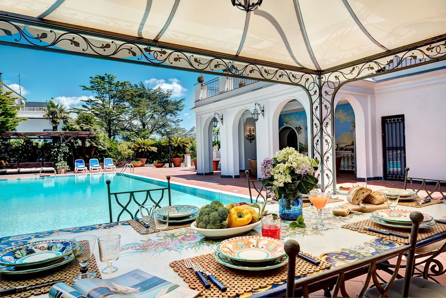 Alfresco dining table set beneath a poolside gazebo.