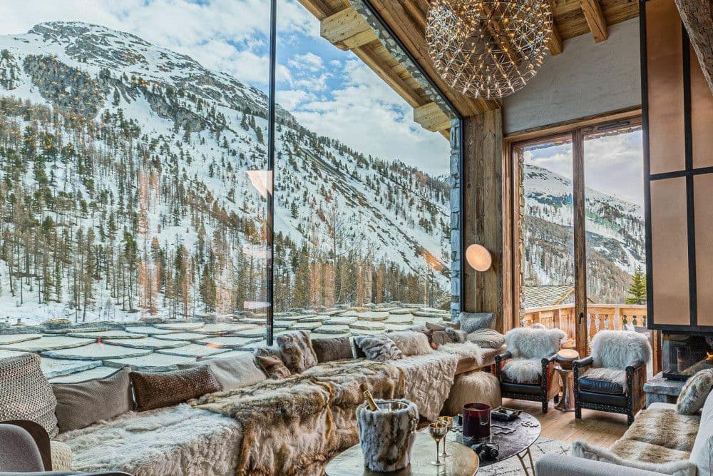 Living room with fur sofas beneath a full-height window onto snowy peaks at Le Fornet 2