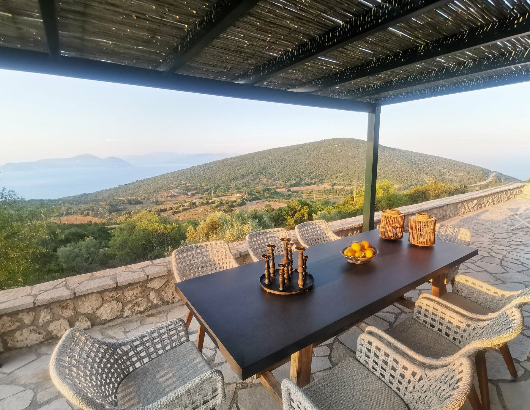 Covered terrace dining table set beneath a pergola with rolling hillside views