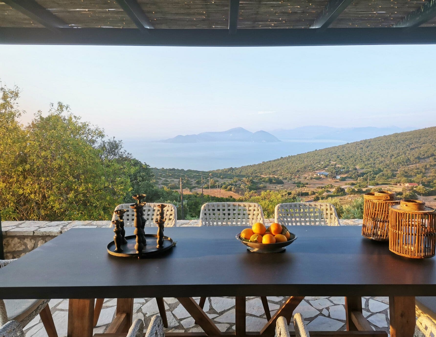 Outdoor dining table laid with fresh fruit and glassware beneath the pergola