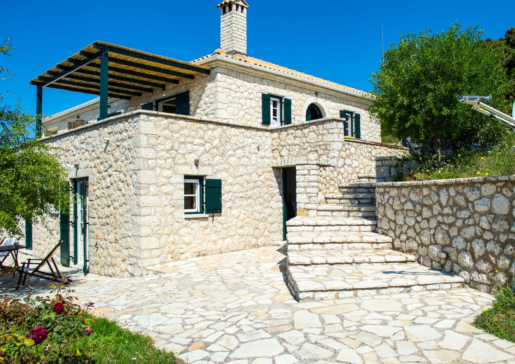 Traditional stone villa facade with dark green shutters against a blue sky