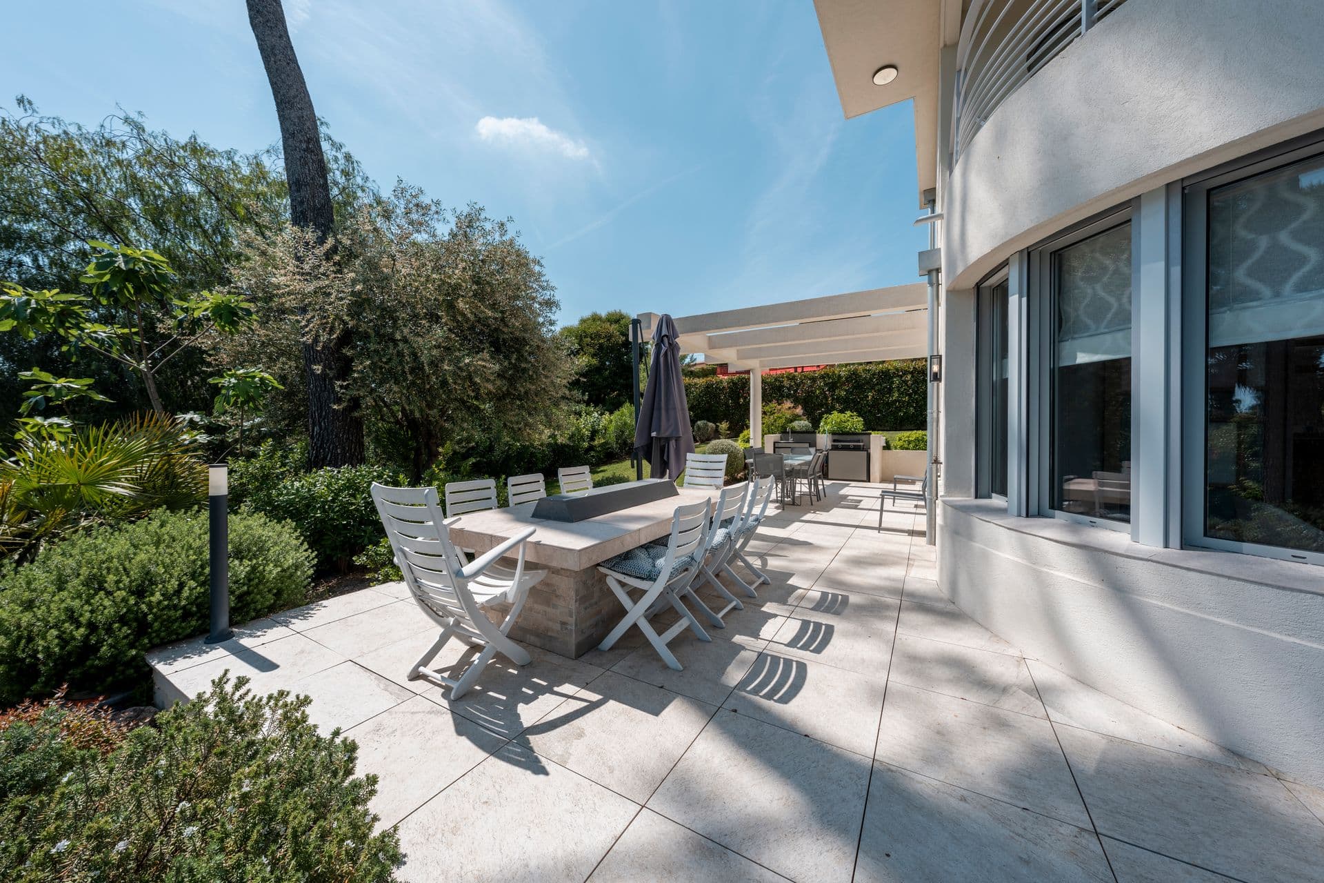 Covered outdoor dining terrace with a long table beside the garden at Above Antibes
