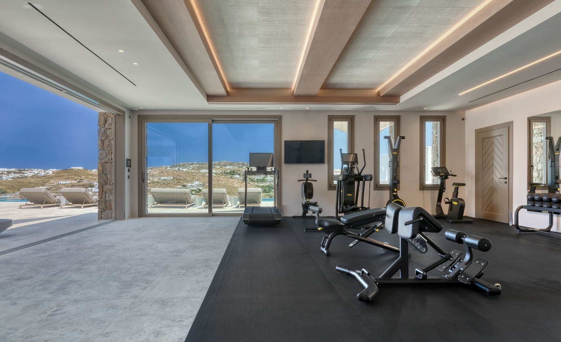 Home gym with cardio and weights equipment opening to the pool terrace at Aegean Aspect, Mykonos